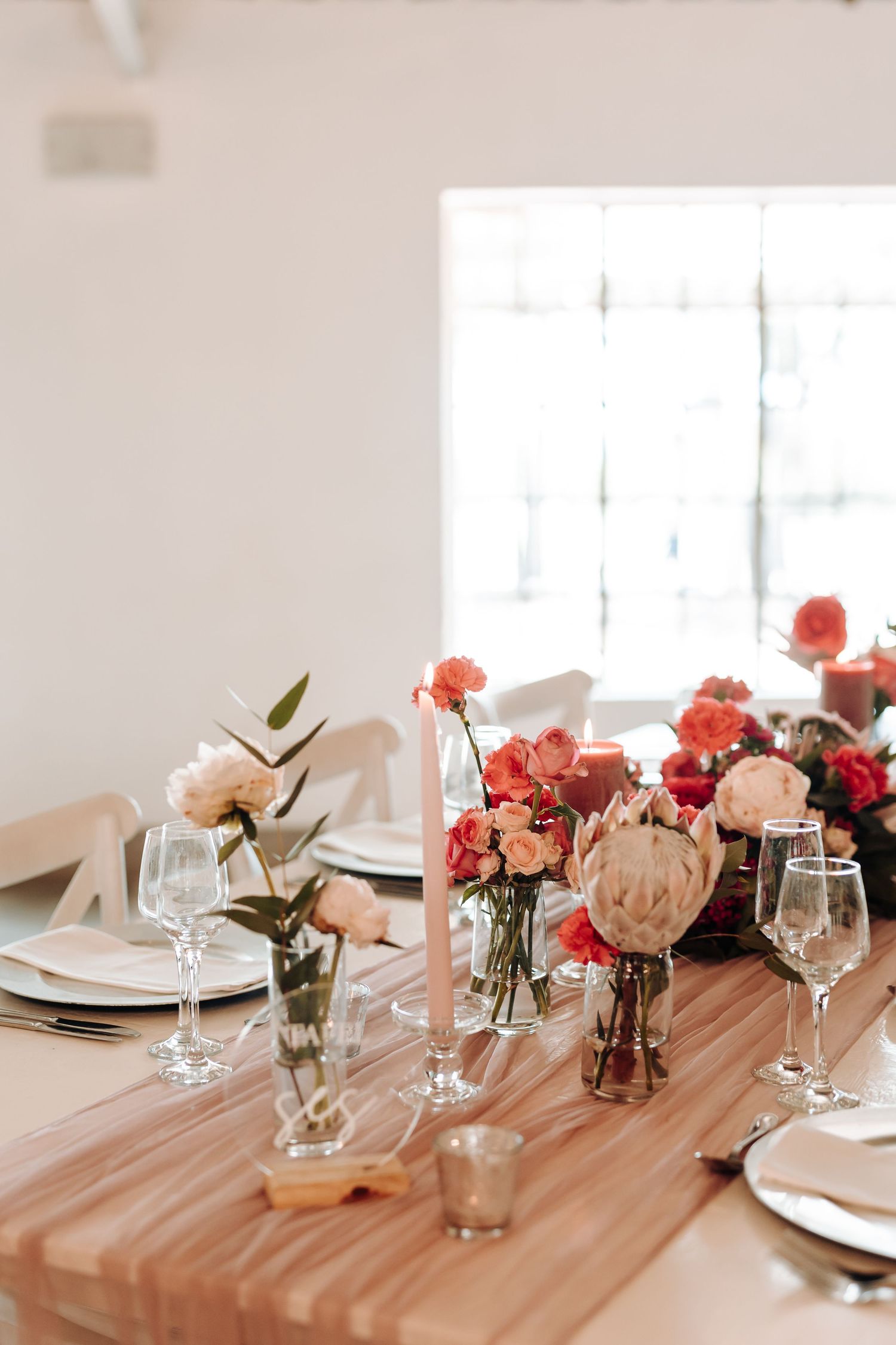 Elegant table setting with pink and coral flowers in small vases on wooden tables.