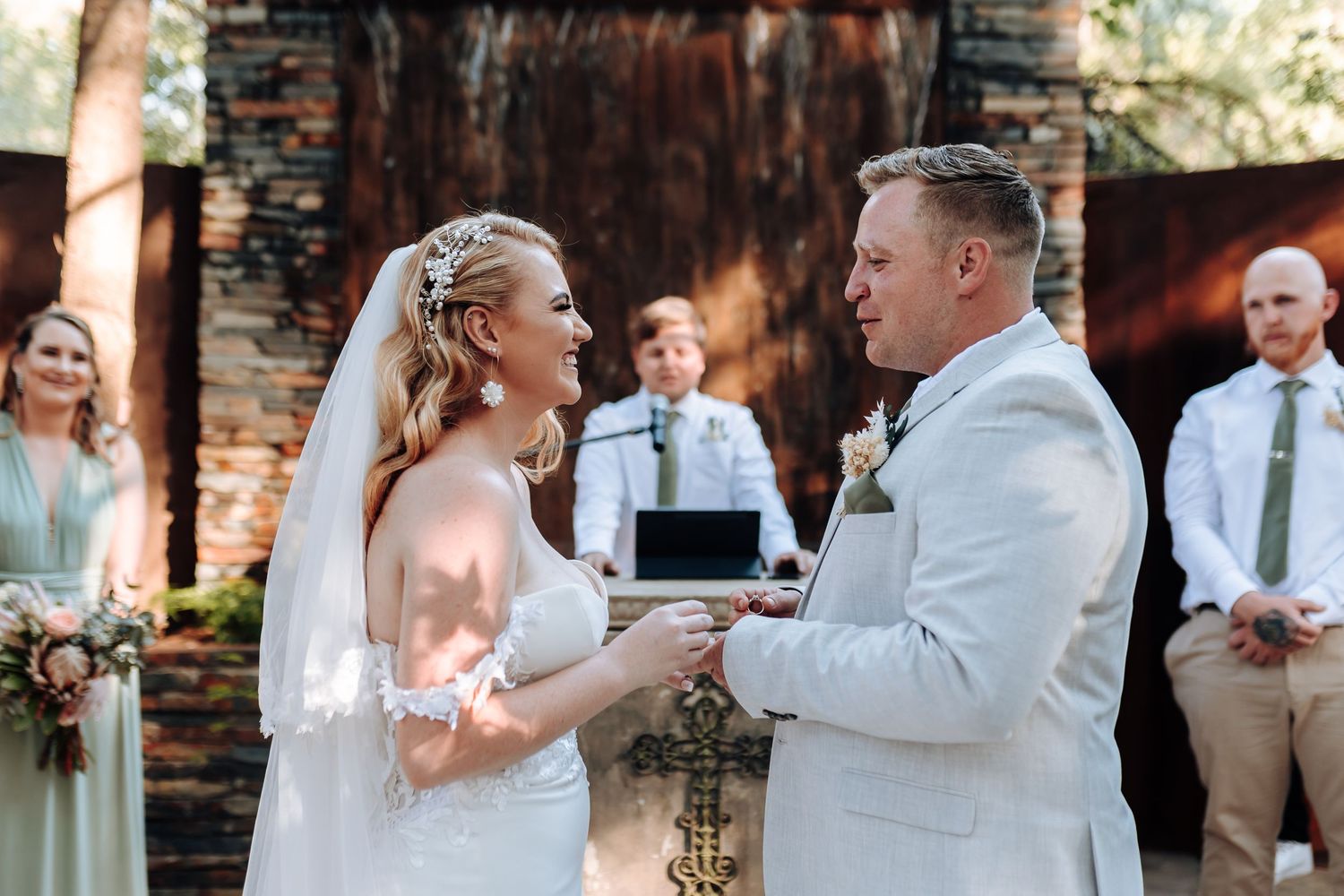 Ring exchange moment during outdoor wedding ceremony against rustic brick backdrop.