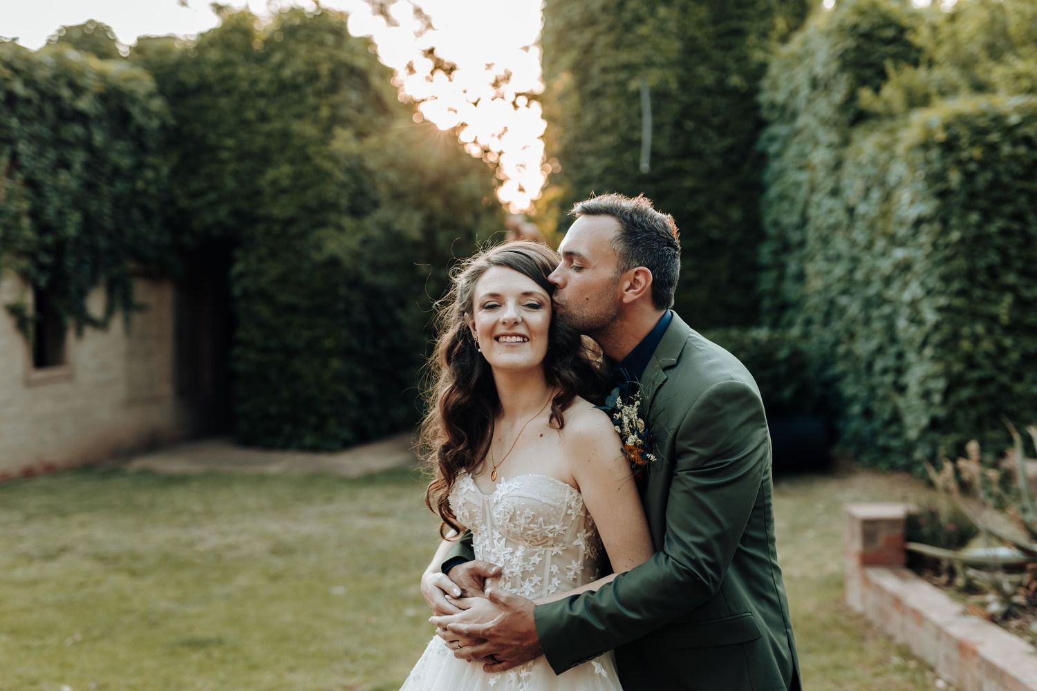 Intimate moment between newlyweds captured against garden backdrop at golden hour.