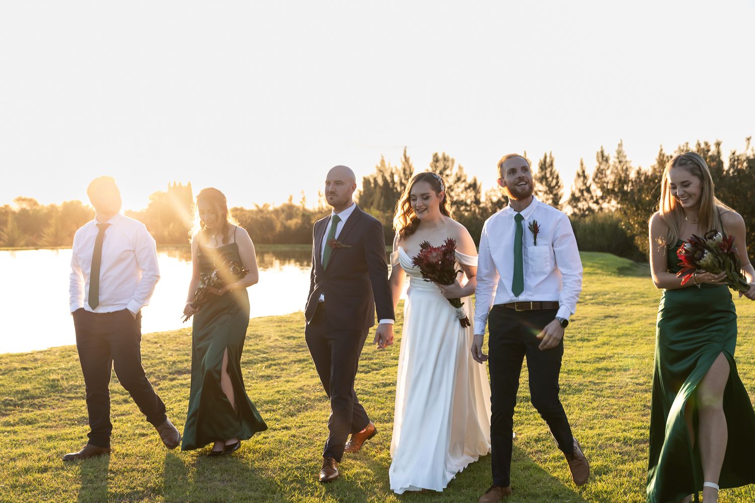 Wedding party dancing and celebrating outdoors during golden hour by the water.