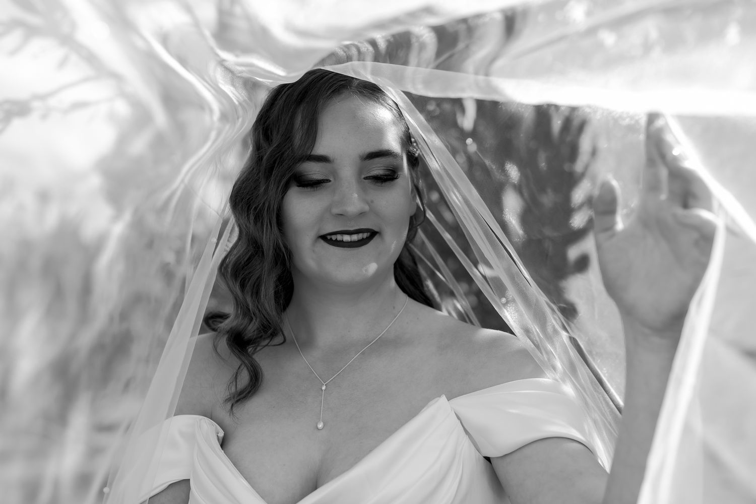 Black and white portrait of bride in off-shoulder gown with delicate veil.