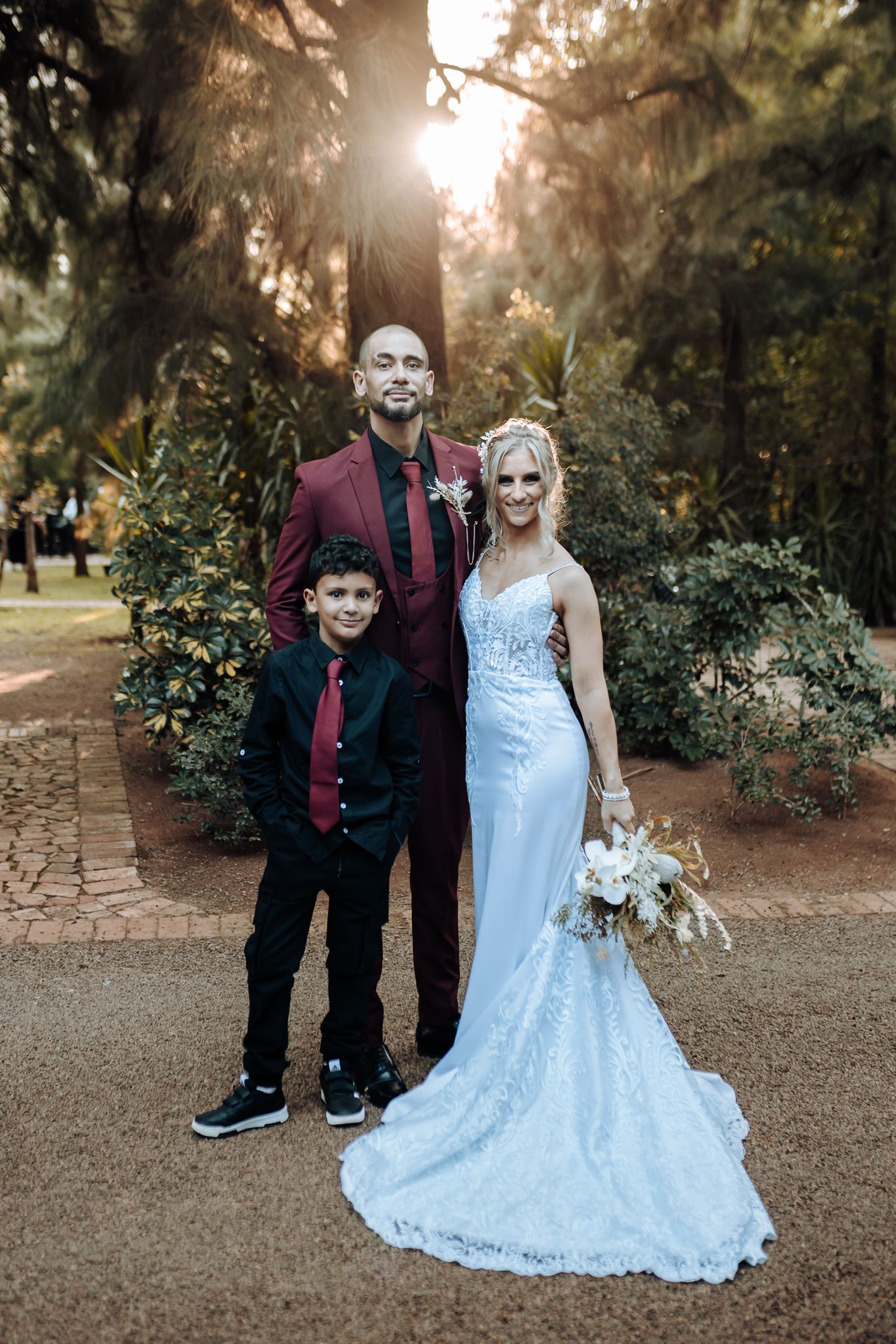 Family in coordinated burgundy and black attire poses for formal wedding portrait at sunset.