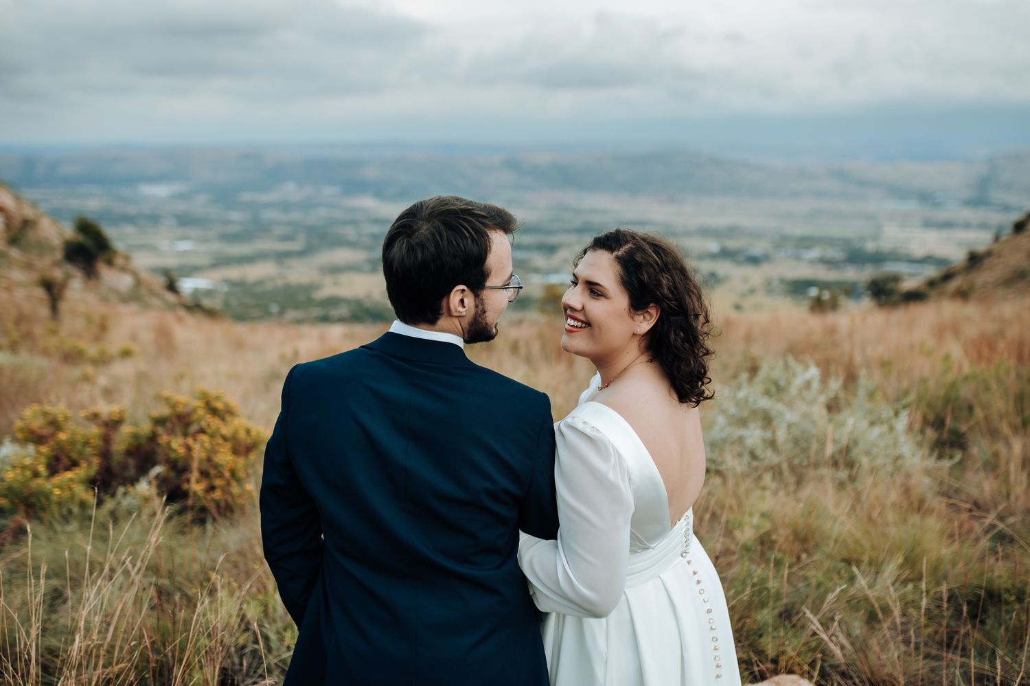 A loving embrace between a couple in wedding attire on a mountainside with valley views.
