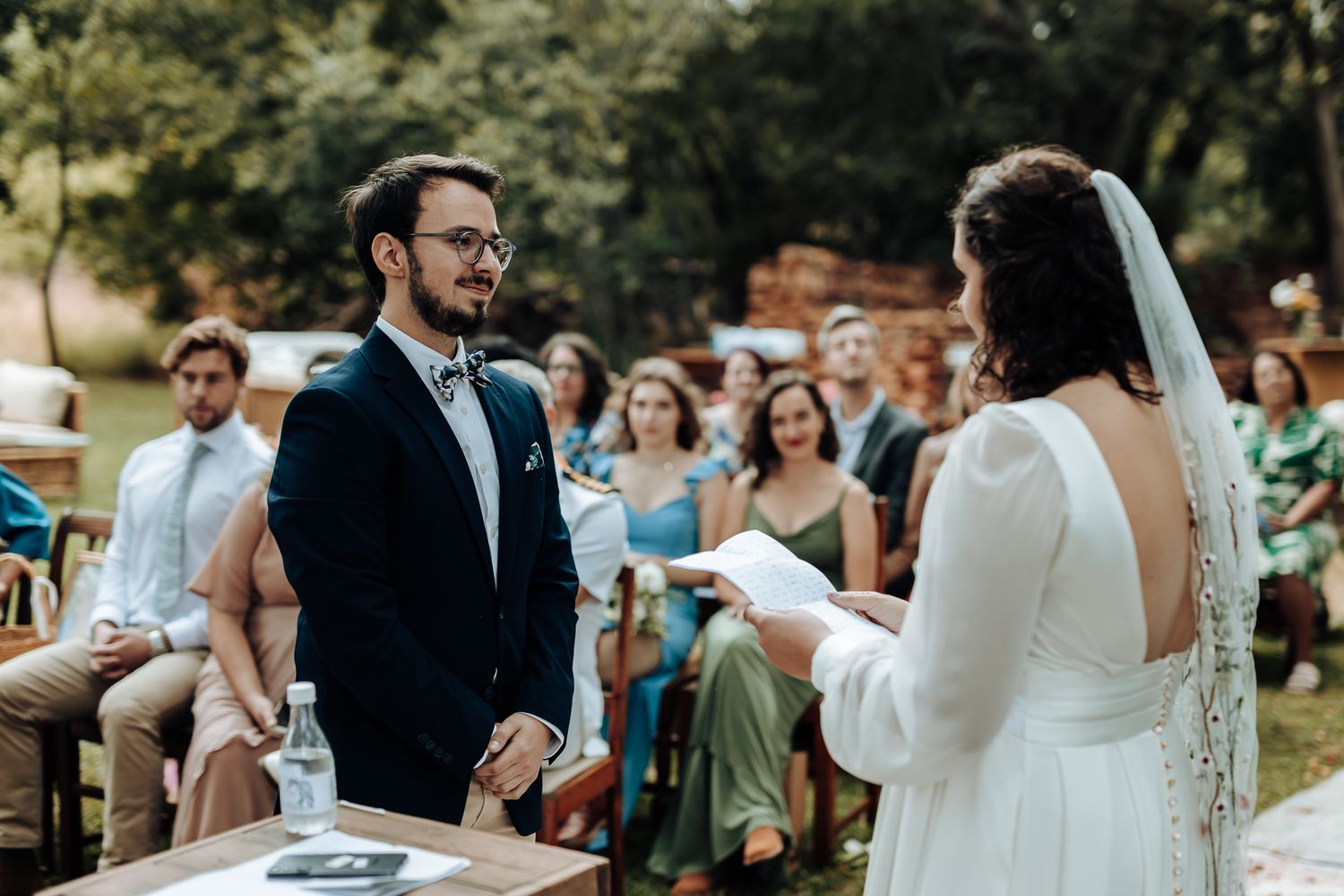 A couple shares vows during their outdoor garden wedding ceremony while guests look on.