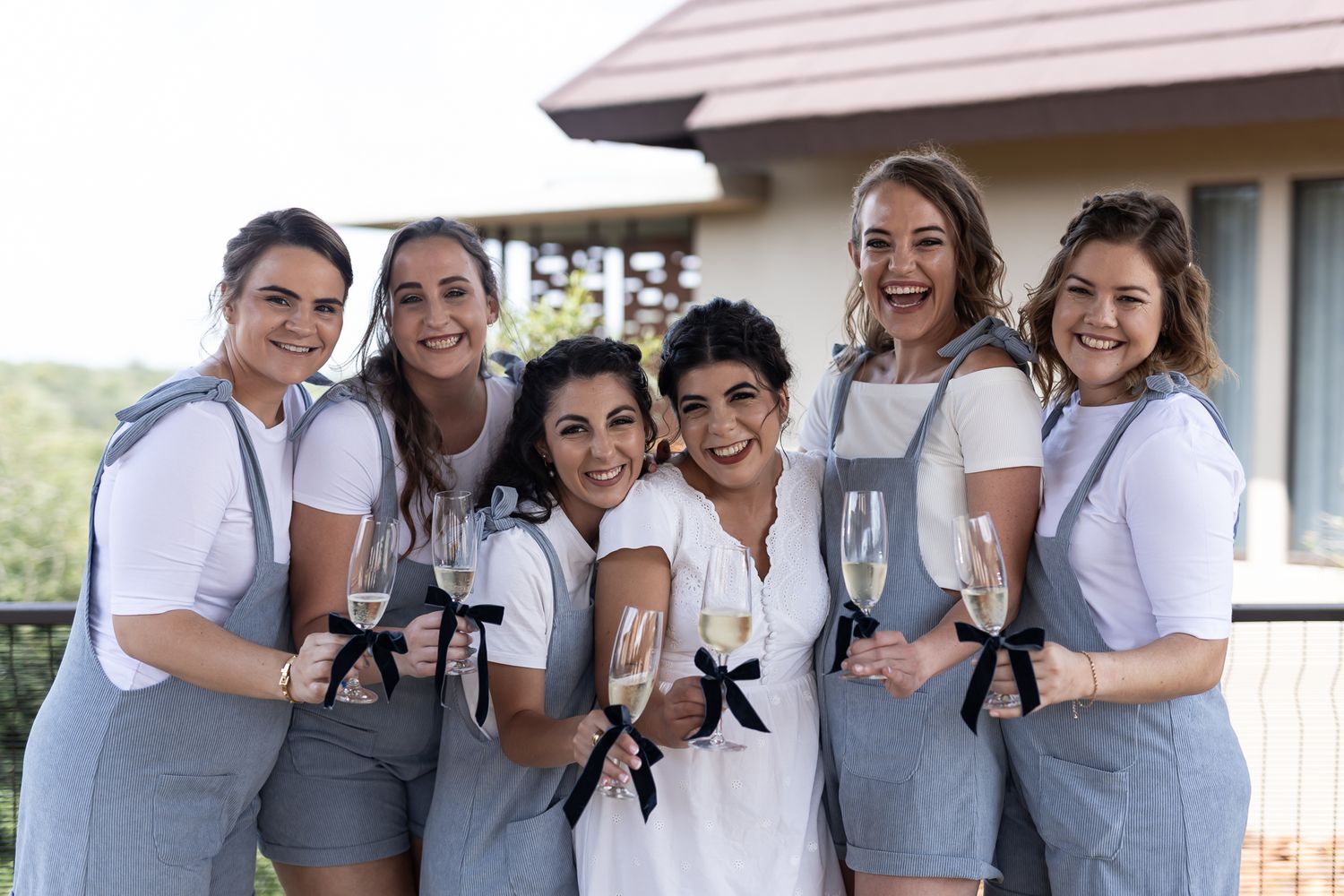 Wedding party in matching gray overalls and white shirts posing on outdoor balcony.