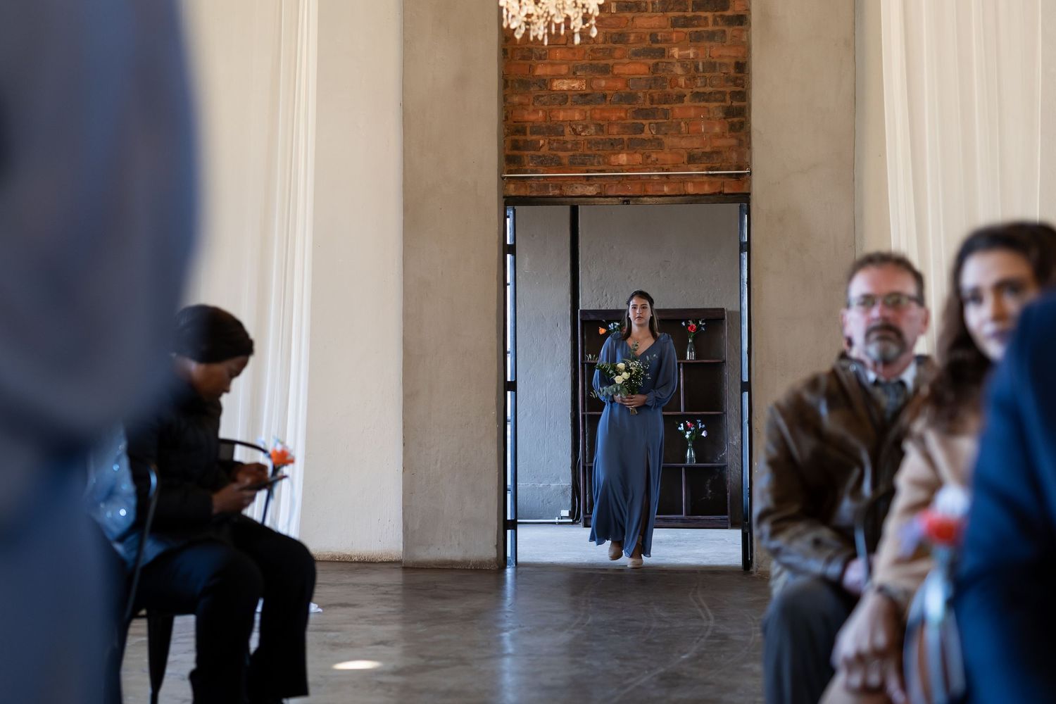 People gather in a modern gallery space with exposed brick walls and white pillars as they view various artworks.