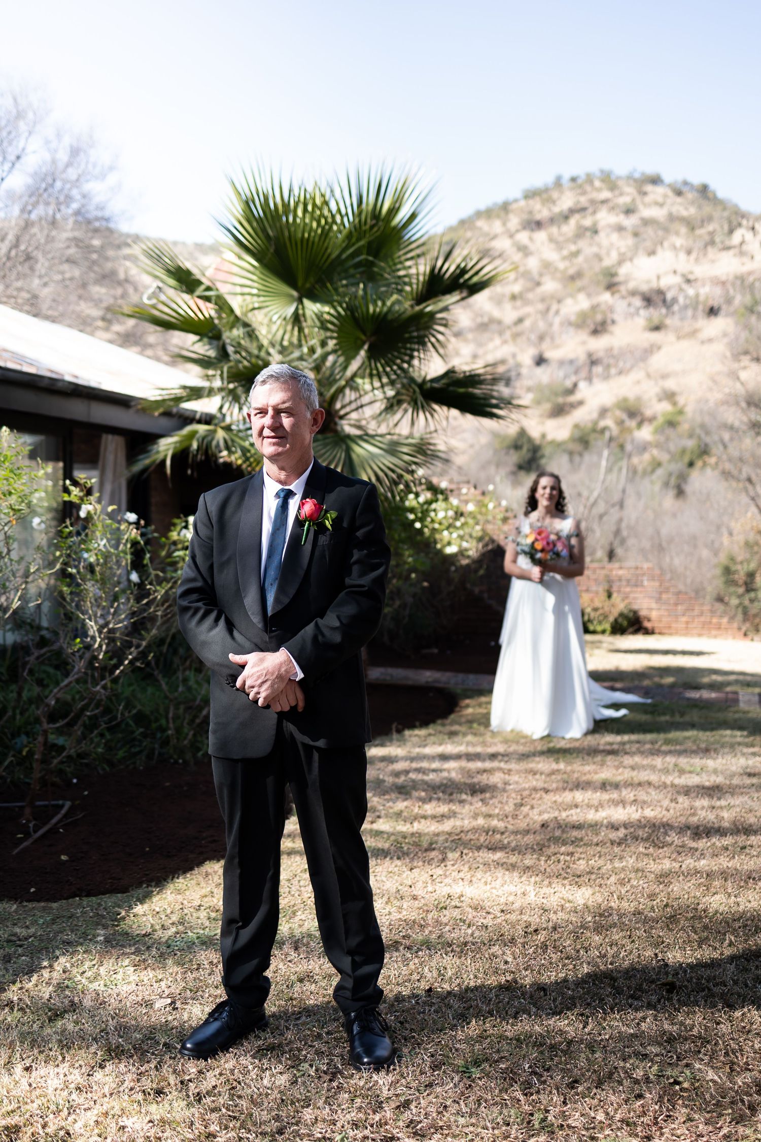 A couple participates in their first look wedding moment outdoors with a palm tree and mountain backdrop.