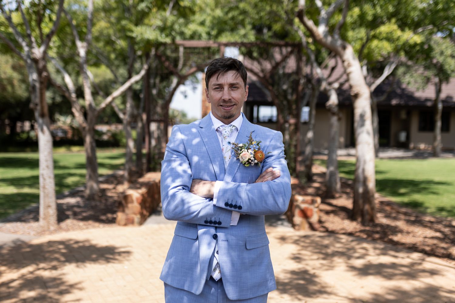 Groom in powder blue suit poses confidently in outdoor garden setting.