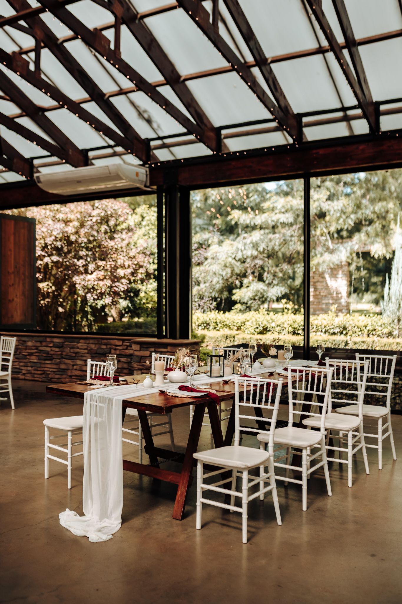 Modern reception venue with white chiavari chairs and glass ceiling overlooking garden views.