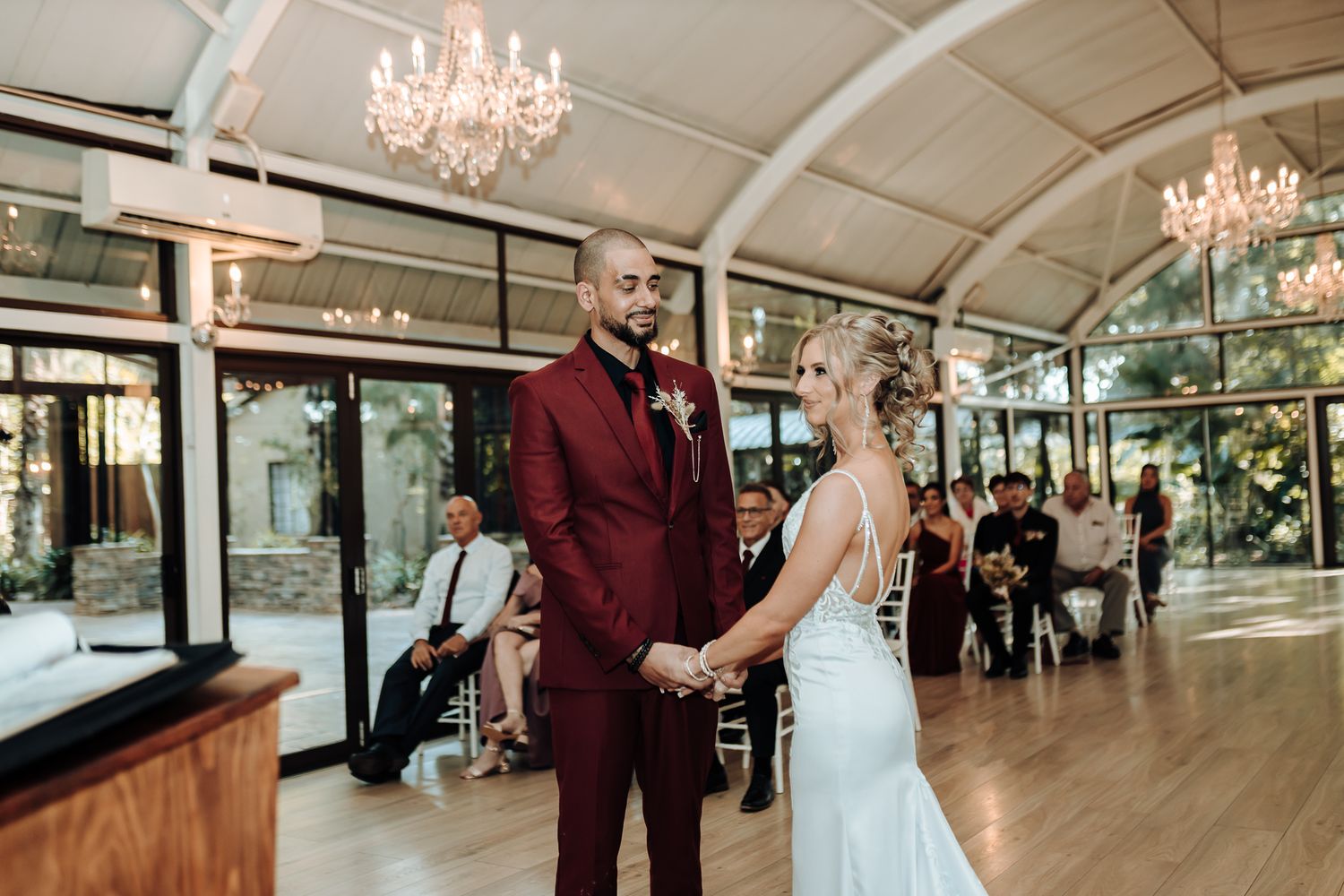 Couple exchanges vows in an elegant venue with natural light streaming through windows.