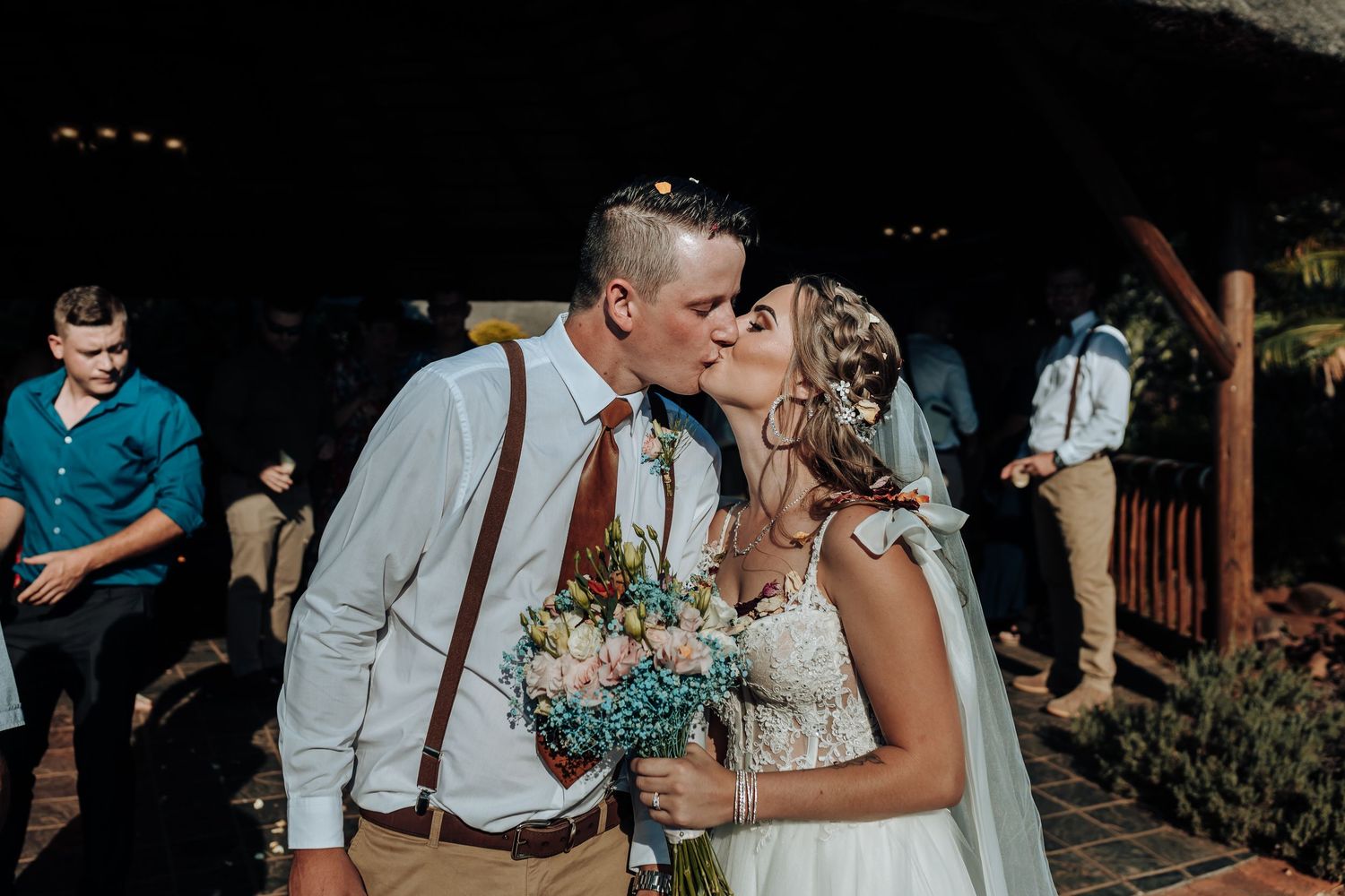 Intimate moment between newlyweds holding bouquet under outdoor pavilion.