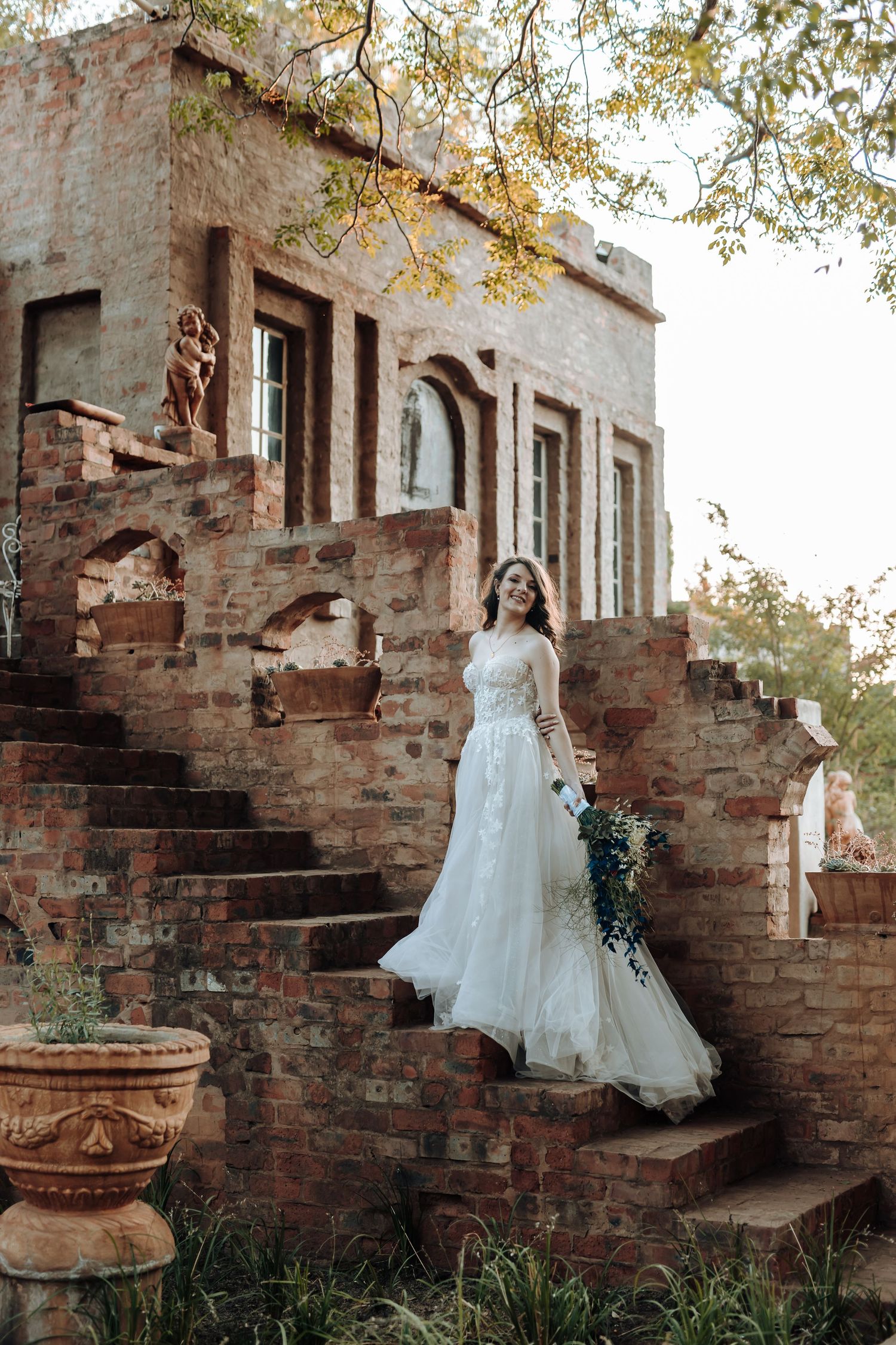 Ethereal bridal portrait on rustic stone steps with flowing white gown and garden backdrop.