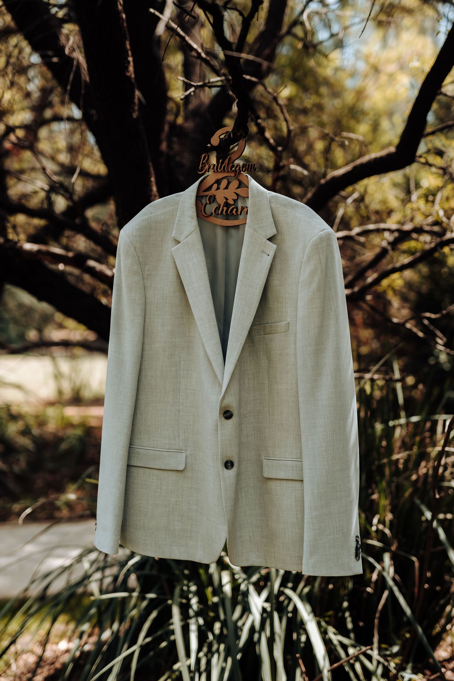 Light beige suit jacket hanging on wooden hanger against natural outdoor background.