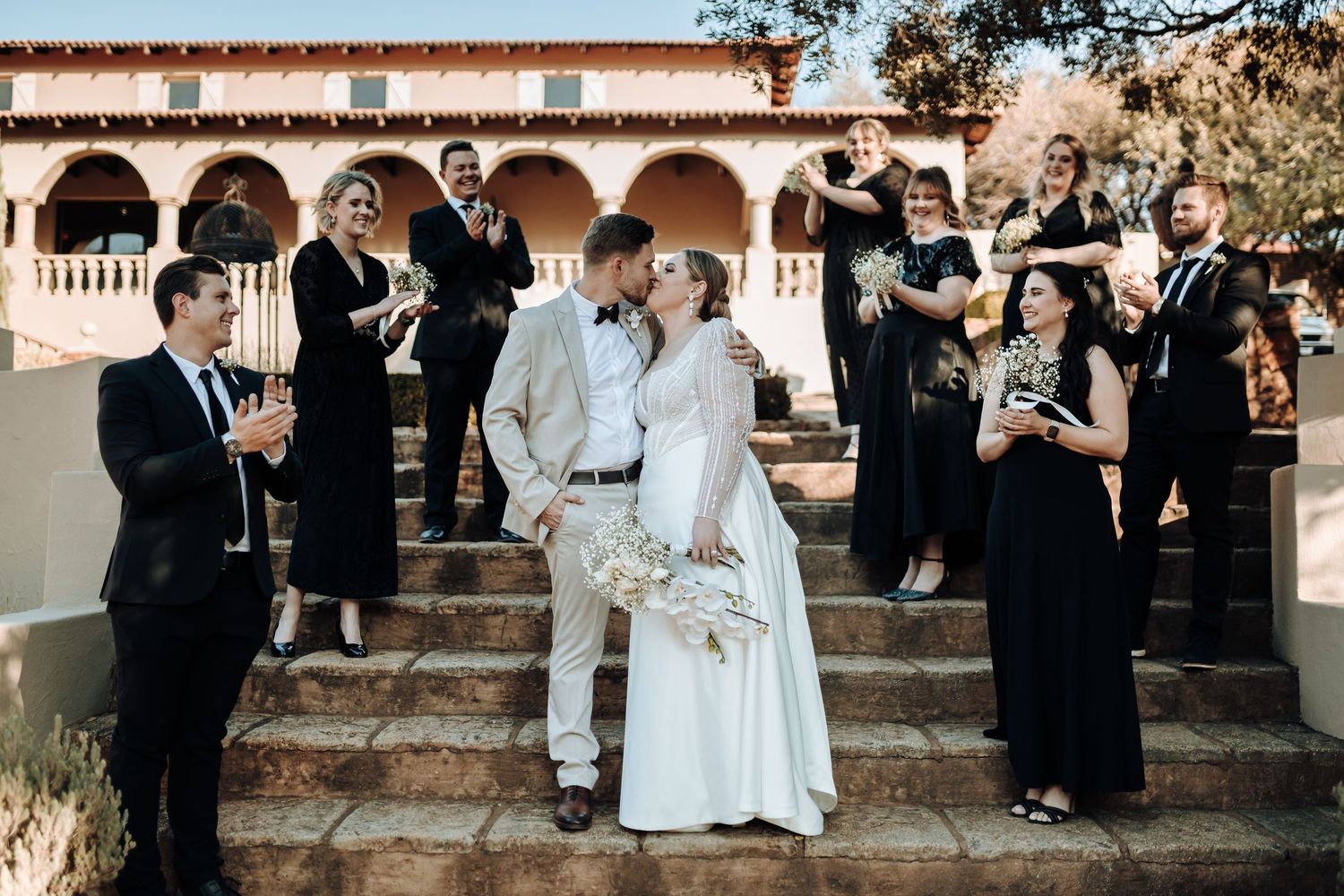 Wedding party celebrates on Mediterranean-style steps with black and white formal attire.