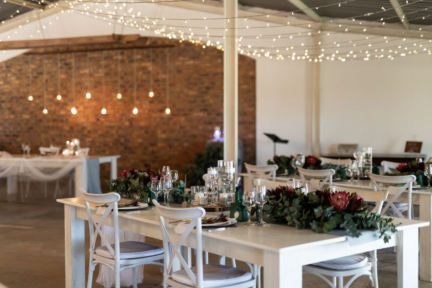 Rustic reception venue with string lights, white chairs, and greenery decorations.