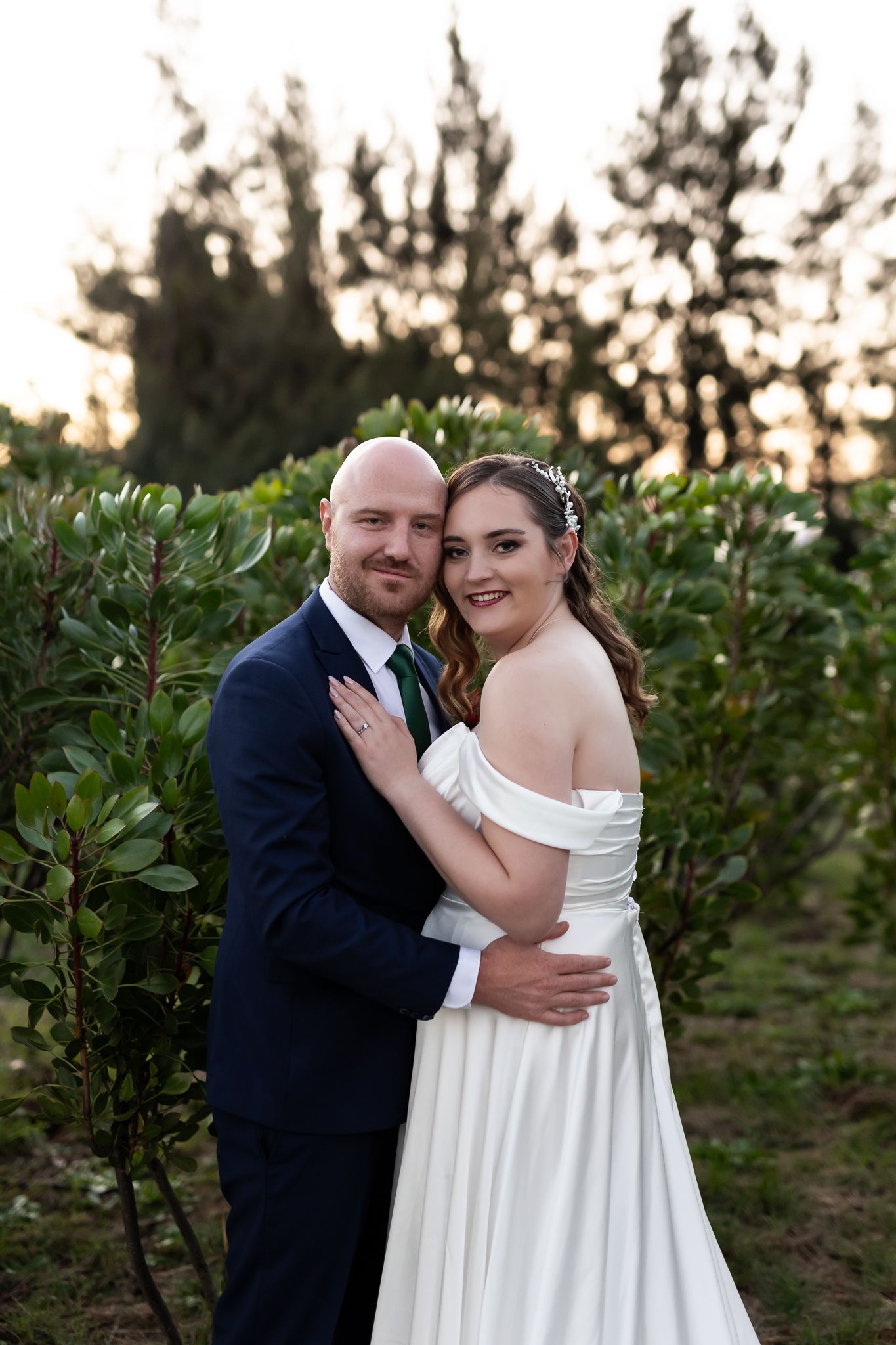 A romantic sunset portrait of newlyweds embracing in a garden setting.