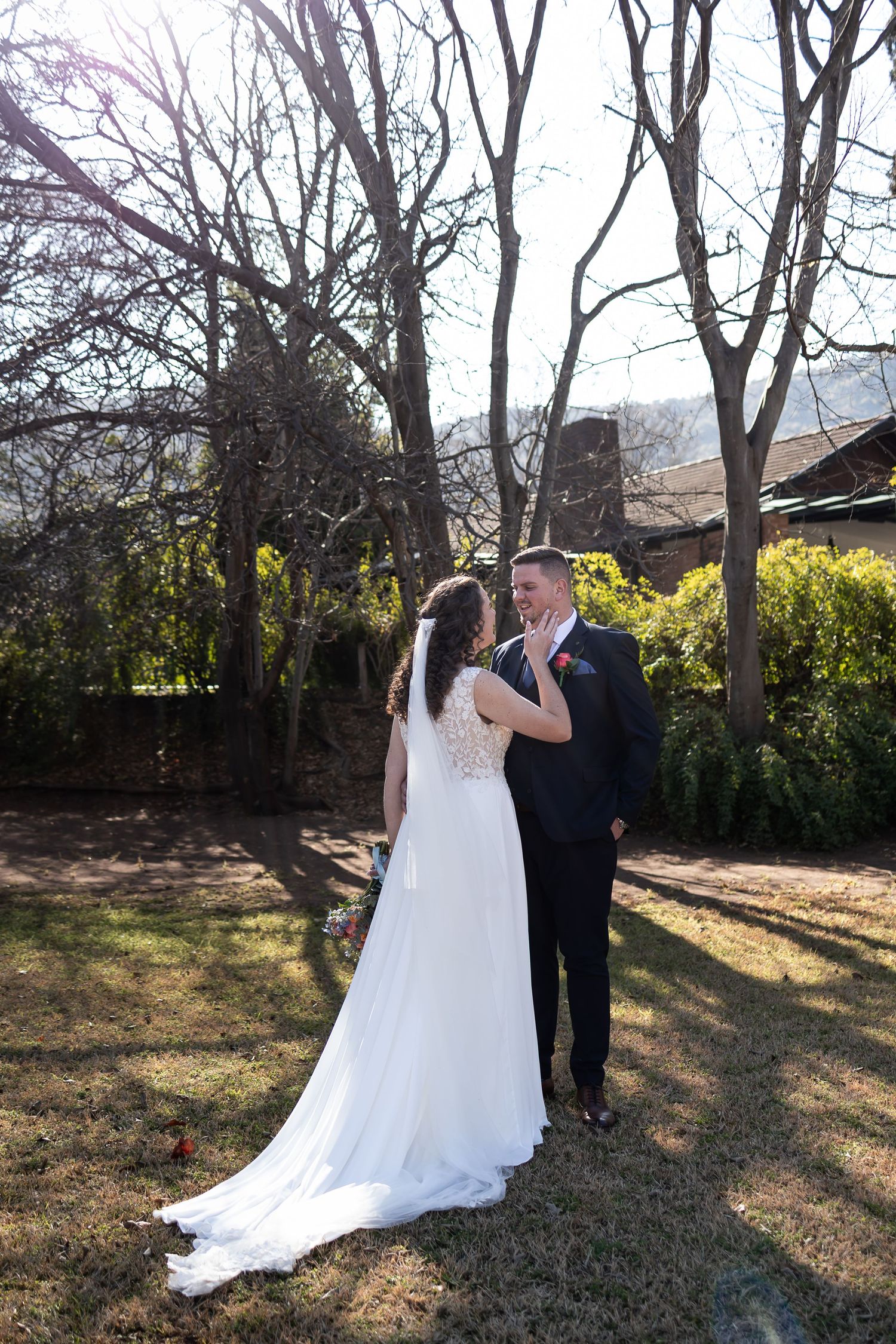 A couple in wedding attire dancing together outside on fallen autumn leaves surrounded by bare trees.