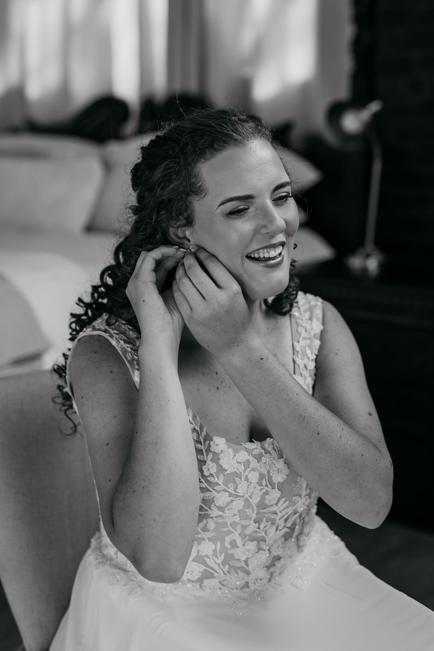 A bride wearing a lace wedding dress laughs joyfully during a candid black and white photography sequence.