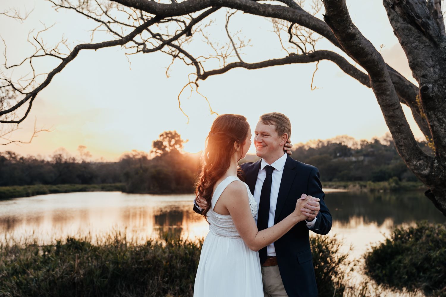 A romantic dance moment at sunset by a serene lake with bare trees framing the scene.