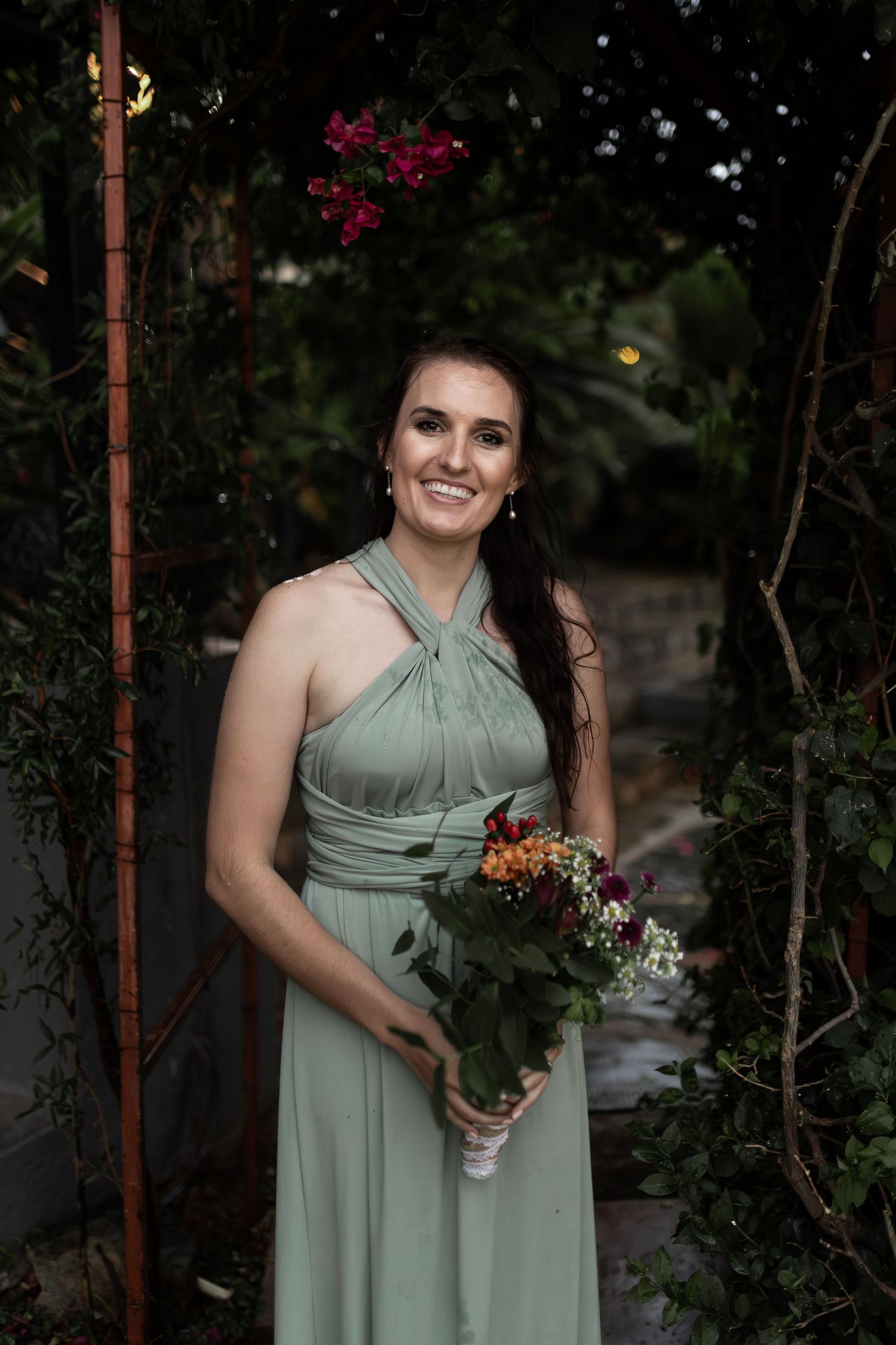 Bridesmaid in sage green halter dress holding autumn-toned floral bouquet.