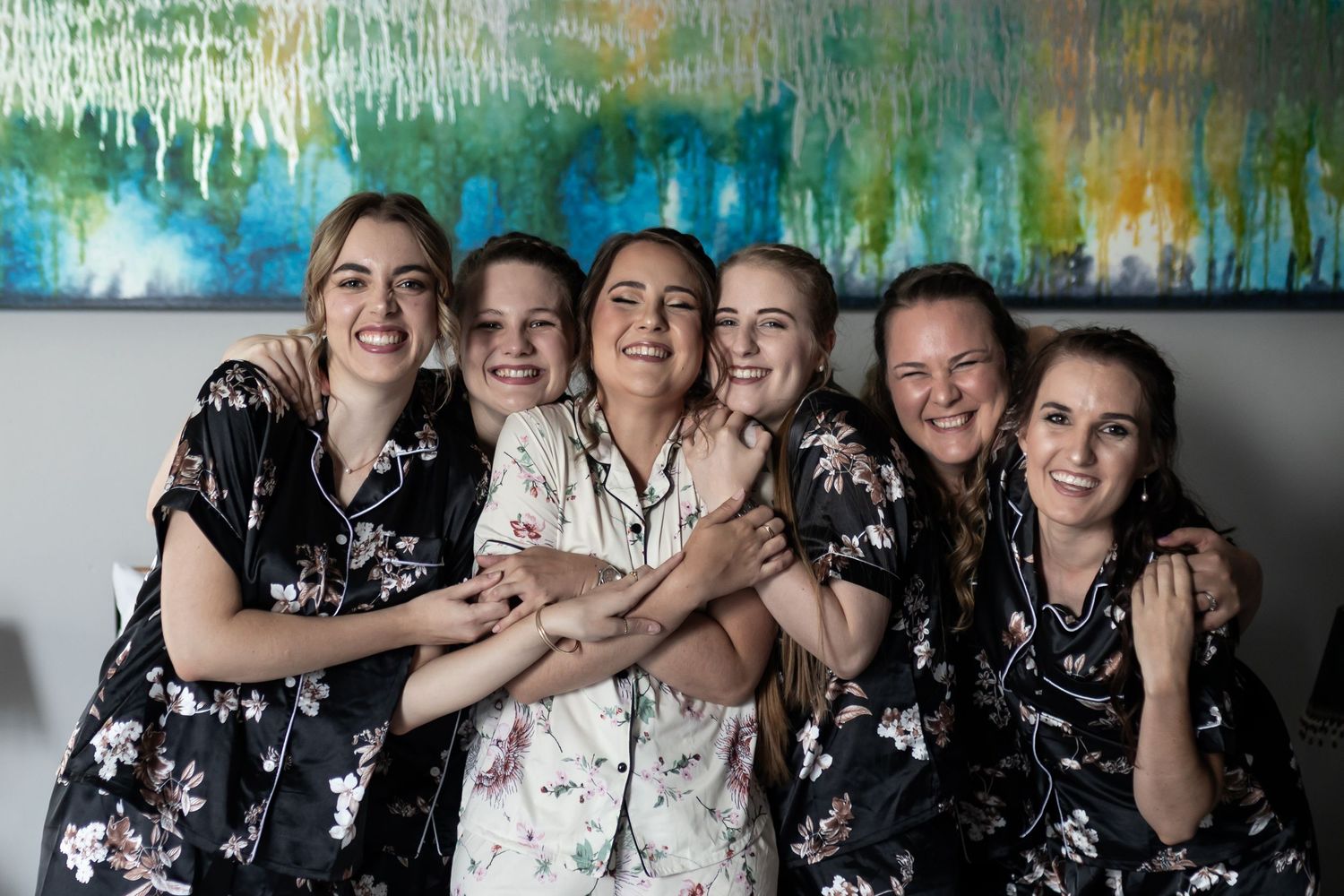 Group wearing matching floral robes pose together against abstract wall art background.