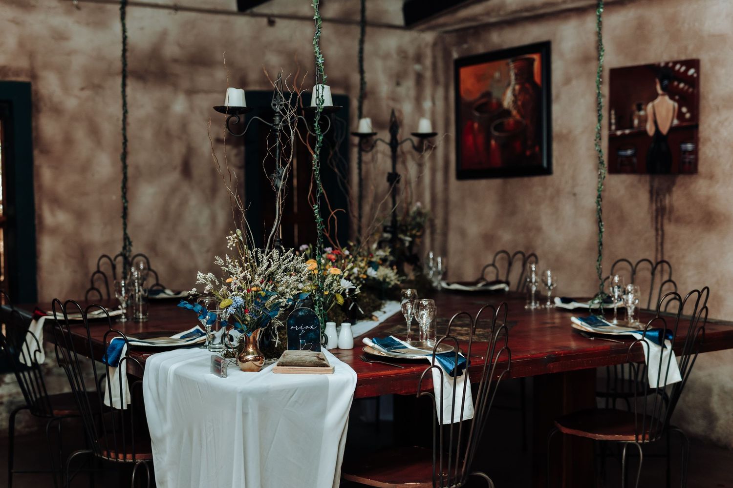 Elegant table setting in rustic venue with floral centerpiece and chandeliers.