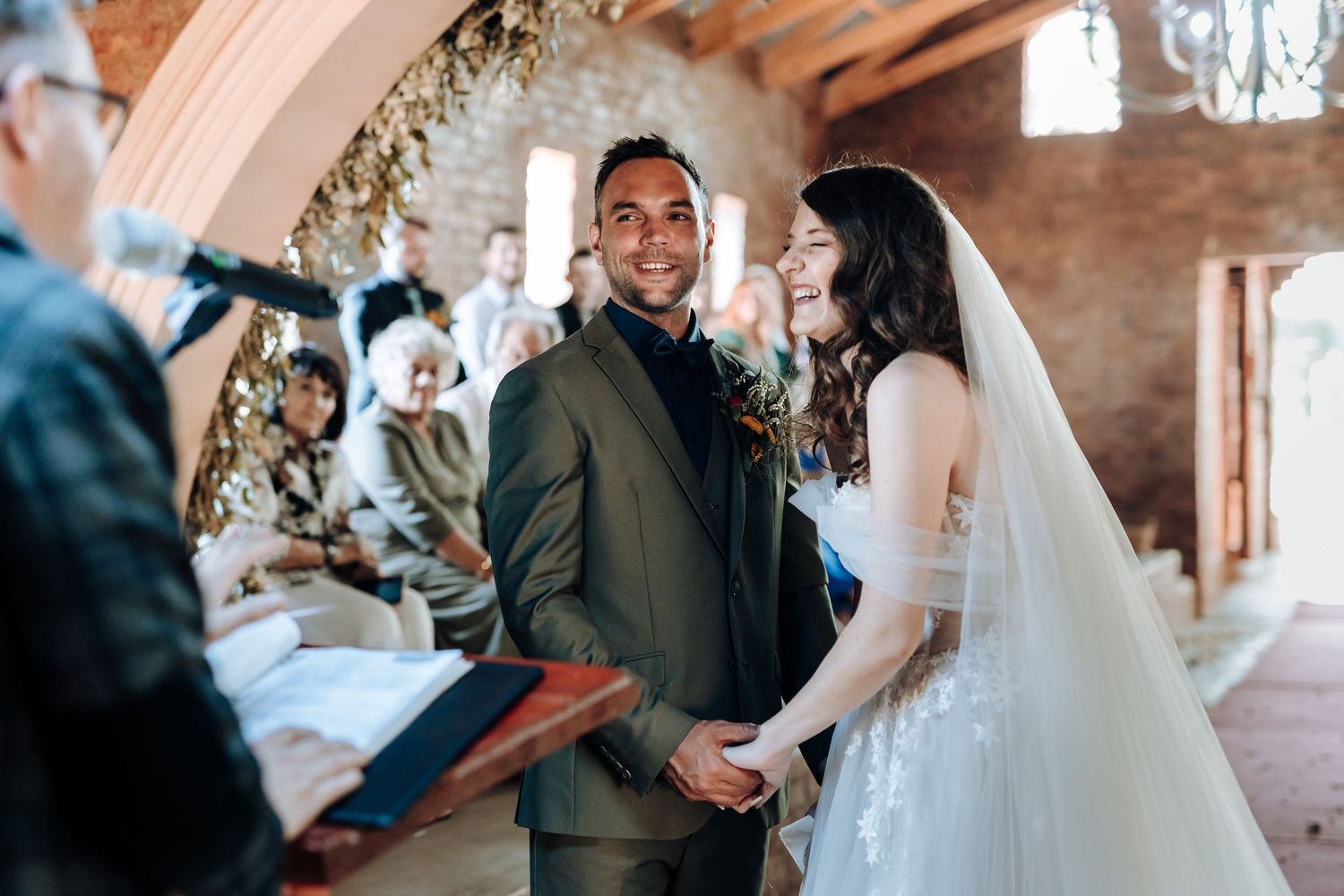 Happy couple exchanges vows during wedding ceremony in rustic brick venue with floral decorations.