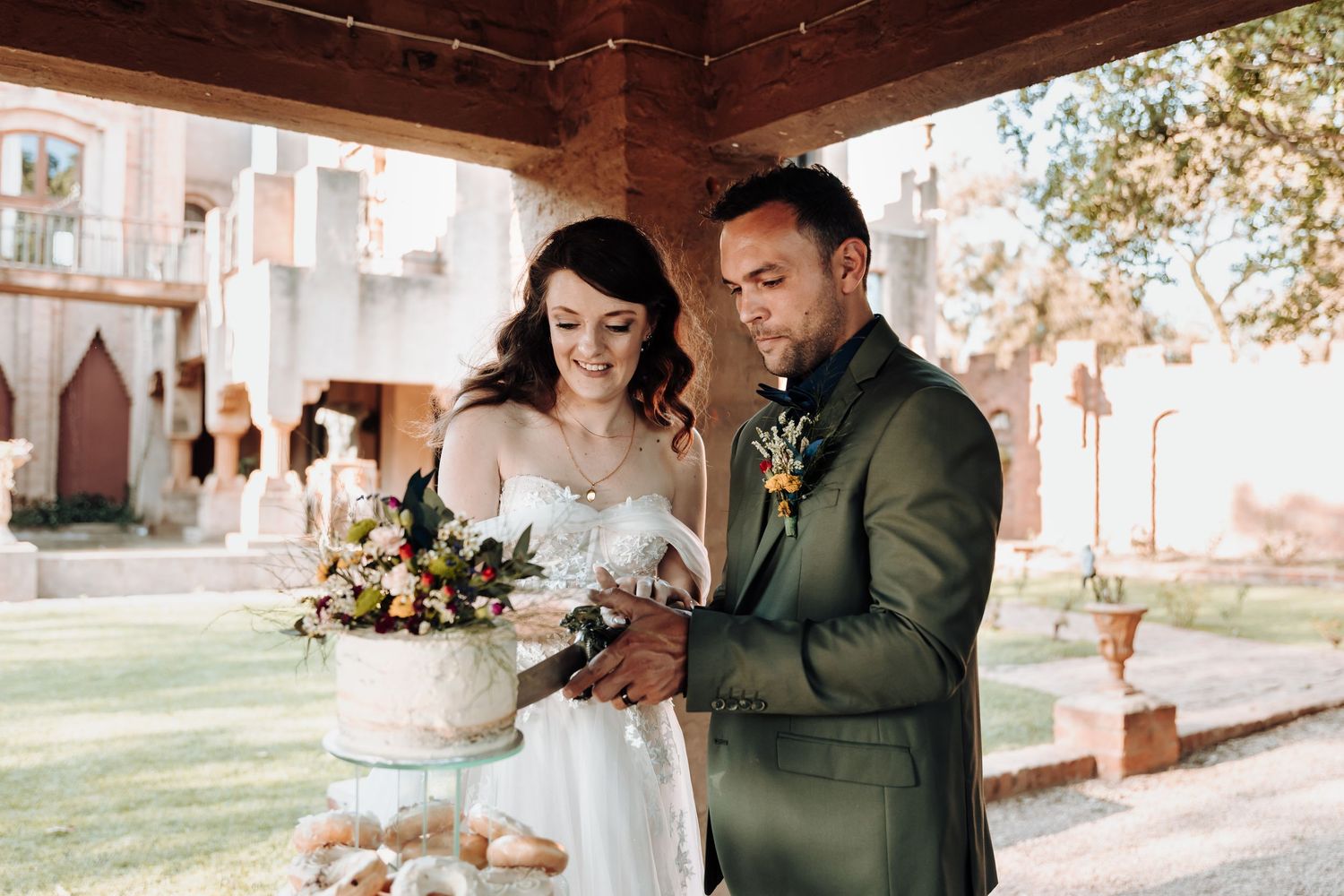 Newlyweds share a joyful moment while cutting their wedding cake at an outdoor reception.