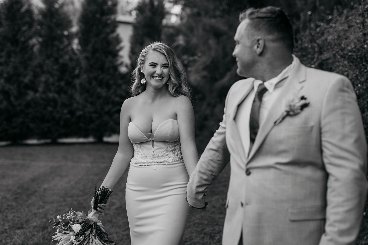 Black and white wedding portrait of couple in formal attire walking outdoors.