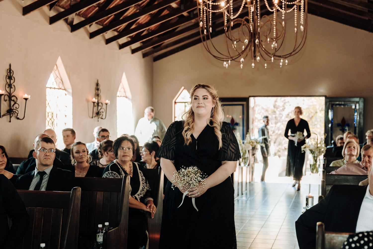 Wedding ceremony in a charming chapel with exposed wooden beams and arched windows illuminated by elegant chandeliers.