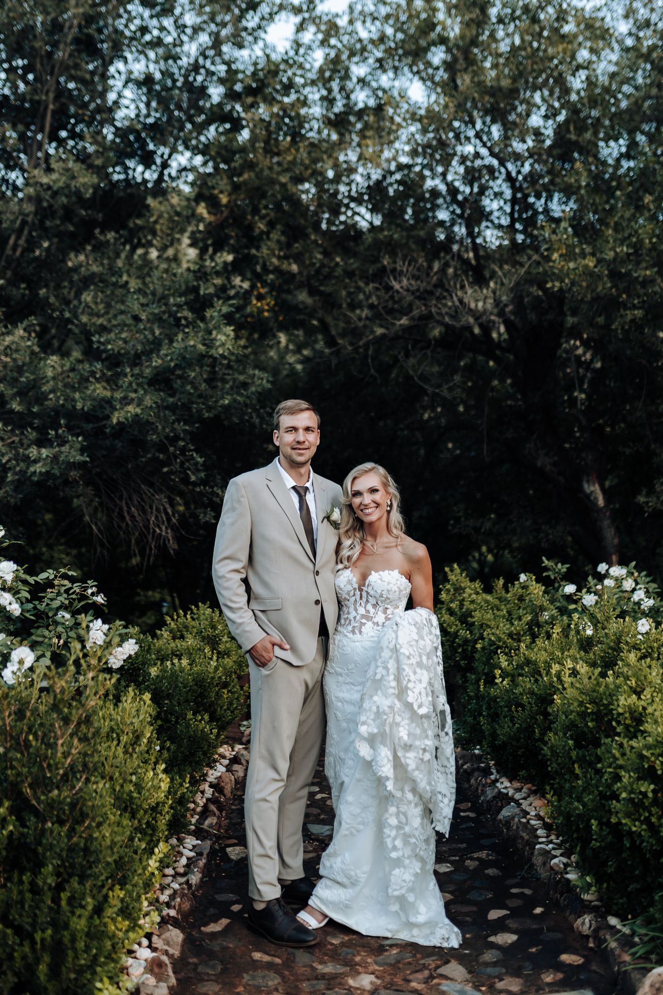 Formal wedding portrait in garden setting with light gray suit and lace gown.