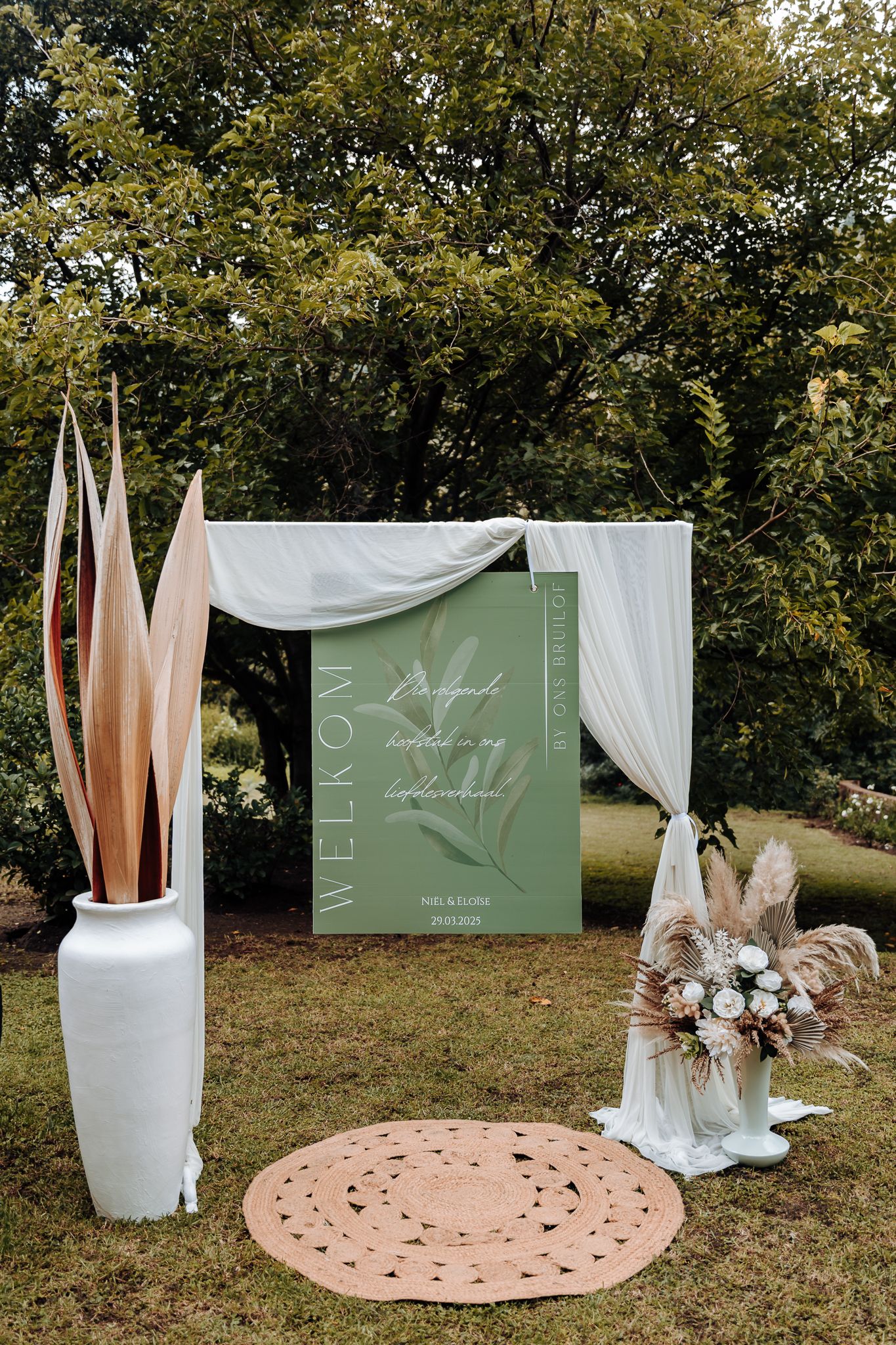 Modern wedding ceremony setup with sage green signage and dried floral arrangements.