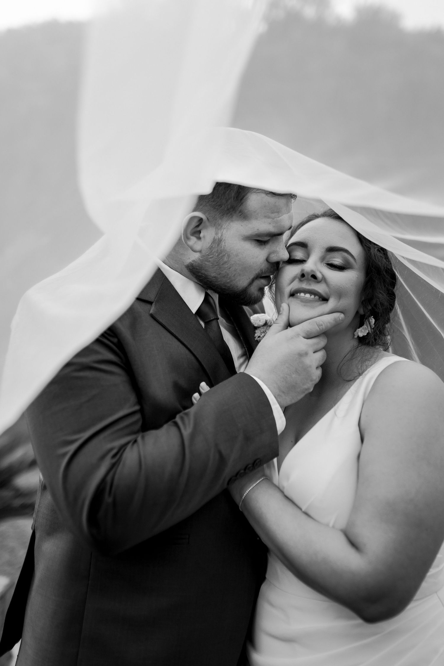 Intimate black and white moment under flowing veil with string lights in background.