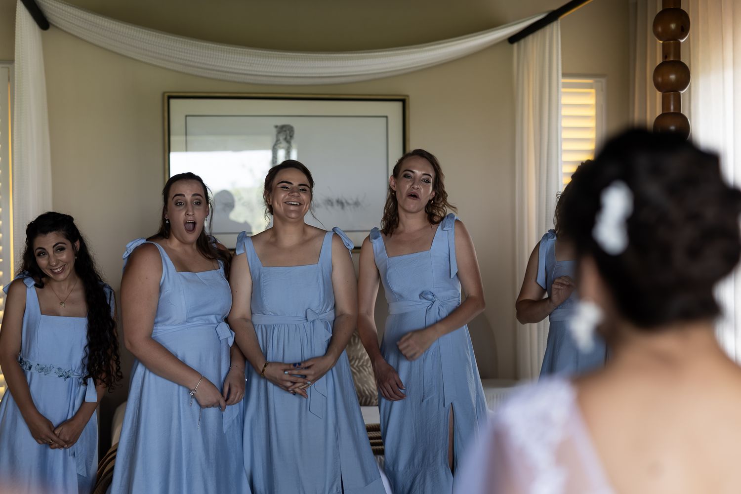 Bridesmaids in light blue dresses gather together in a room during wedding preparations.