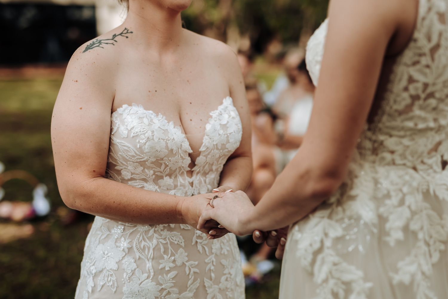 Close-up detail of two white lace wedding dresses during ceremony.