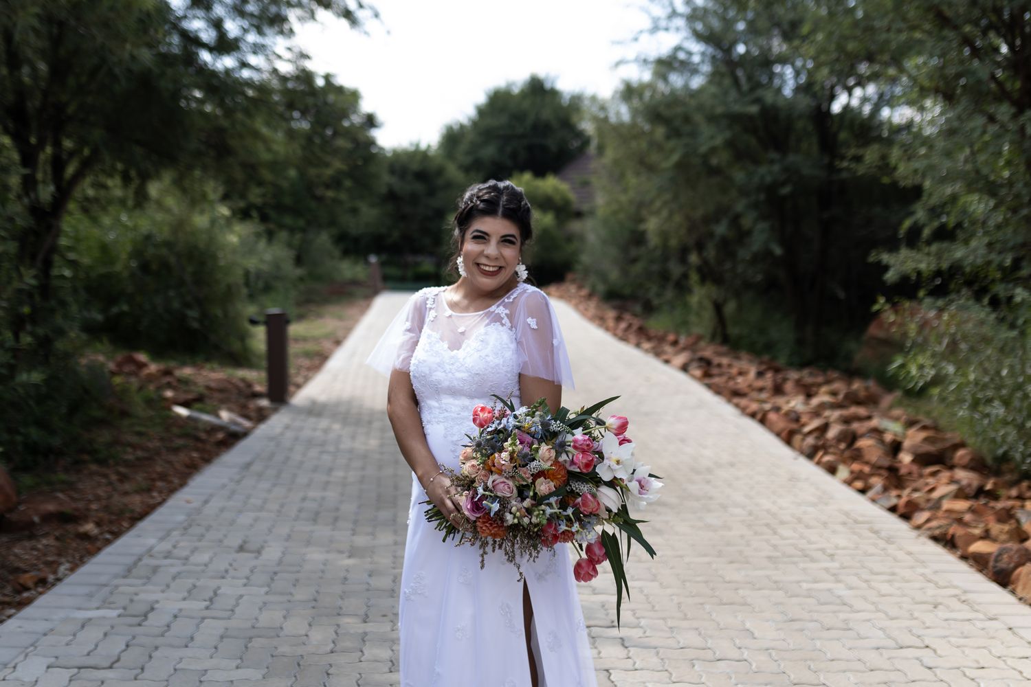 Bride in classic white dress poses on a stone pathway with a colorful bouquet.