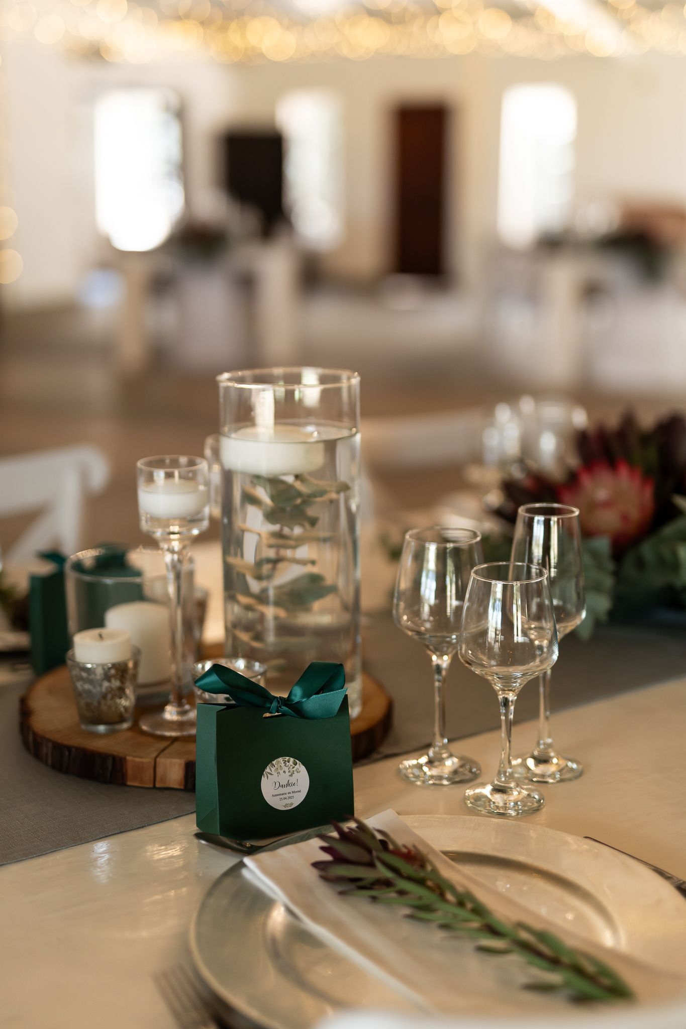 Table setting with floating candles, wine glasses, and emerald green favor boxes.