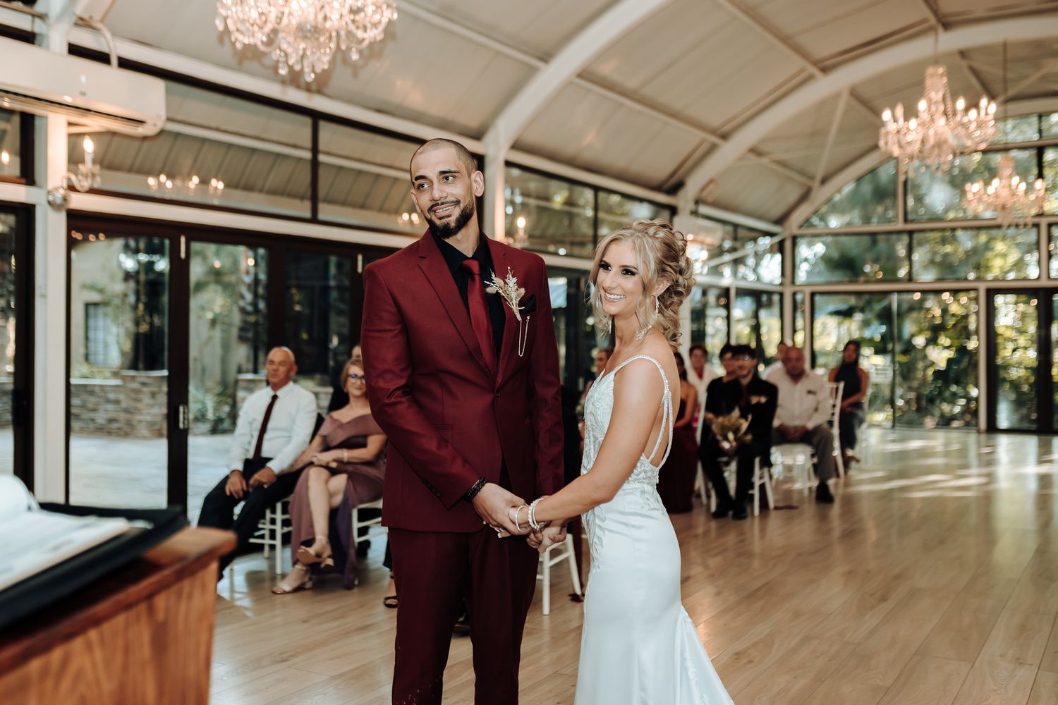 Newlyweds share their first moment in an elegant venue with chandeliers and hardwood floors.