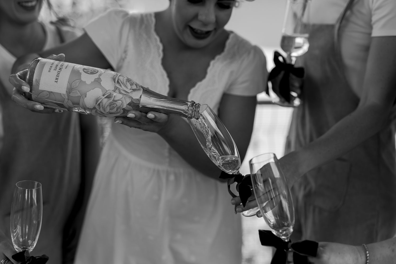 Black and white photo of champagne being poured into wine glasses at a celebration.
