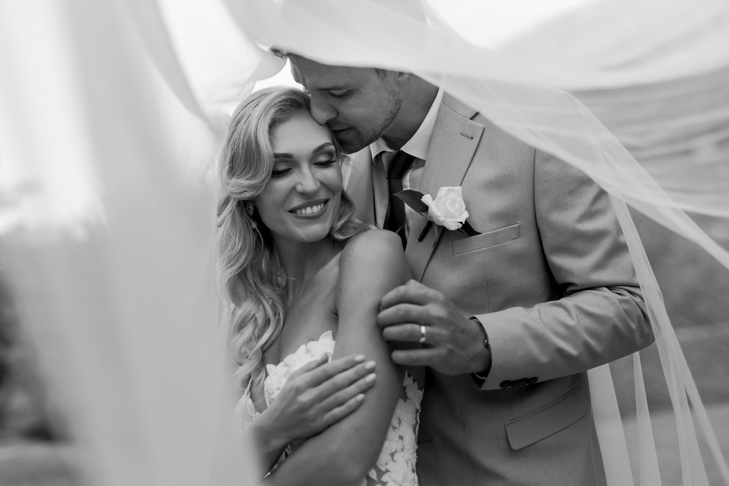 Intimate black and white portrait of a romantic wedding couple embracing under a flowing veil.