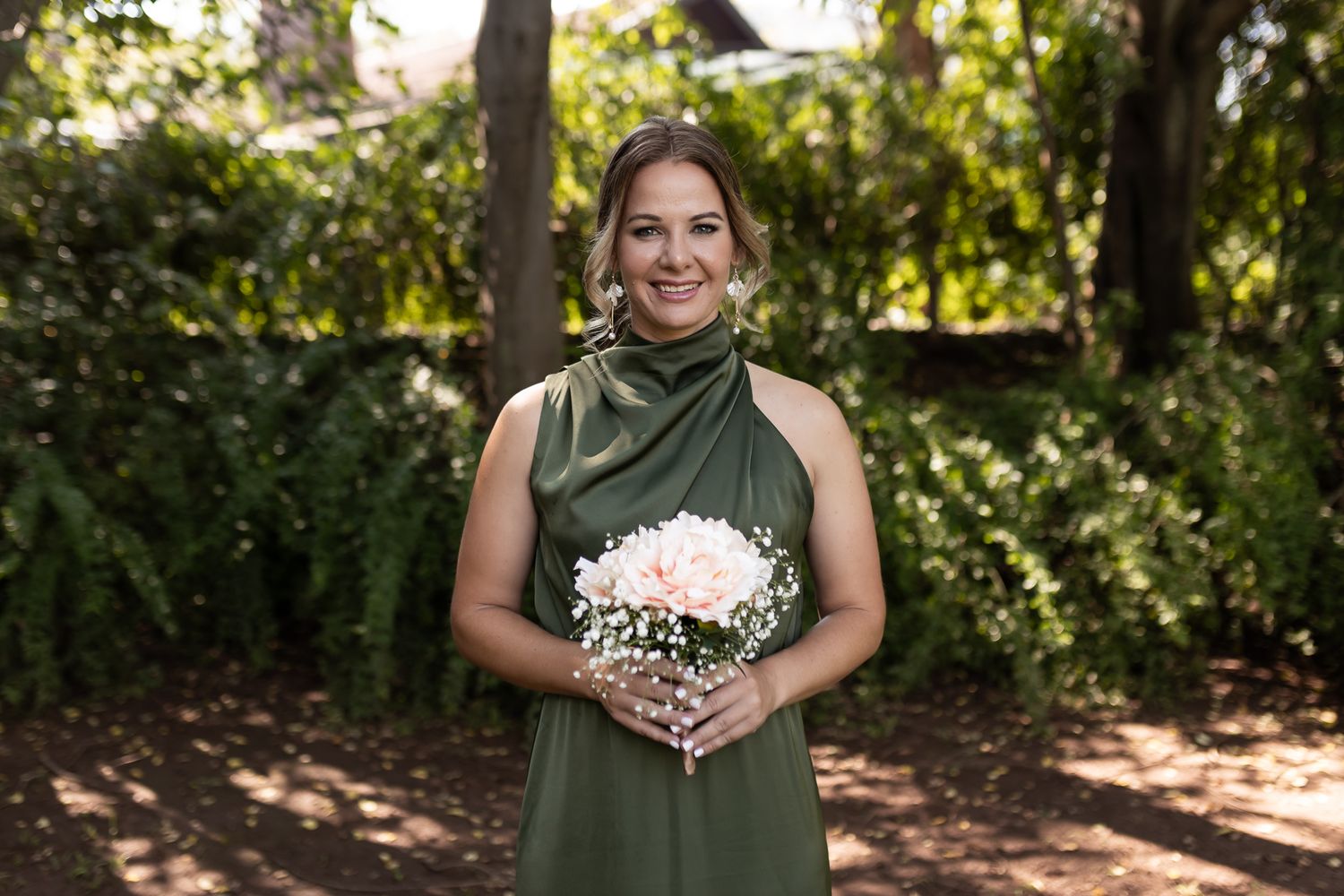 Bridesmaid wearing sage green halter dress smiles while holding white floral bouquet.
