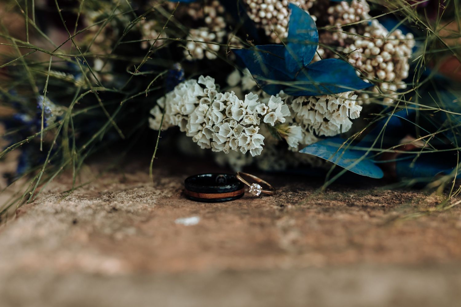 Wedding rings photographed with delicate white flowers and blue accents in macro detail.