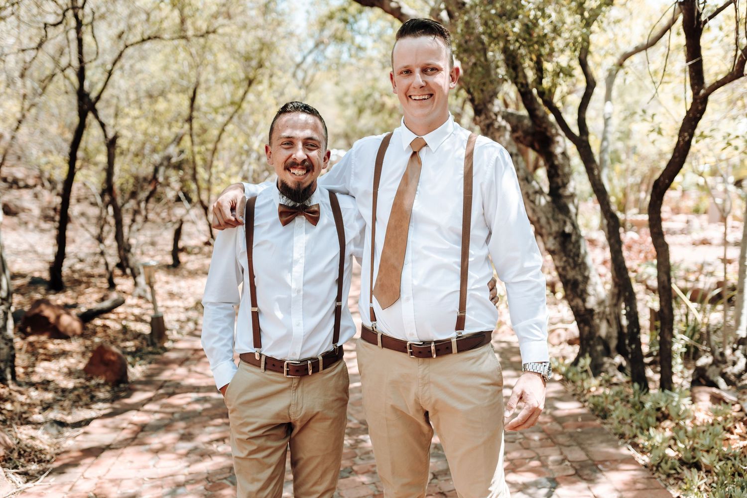 Two people in matching formal wear with suspenders smiling together outdoors.