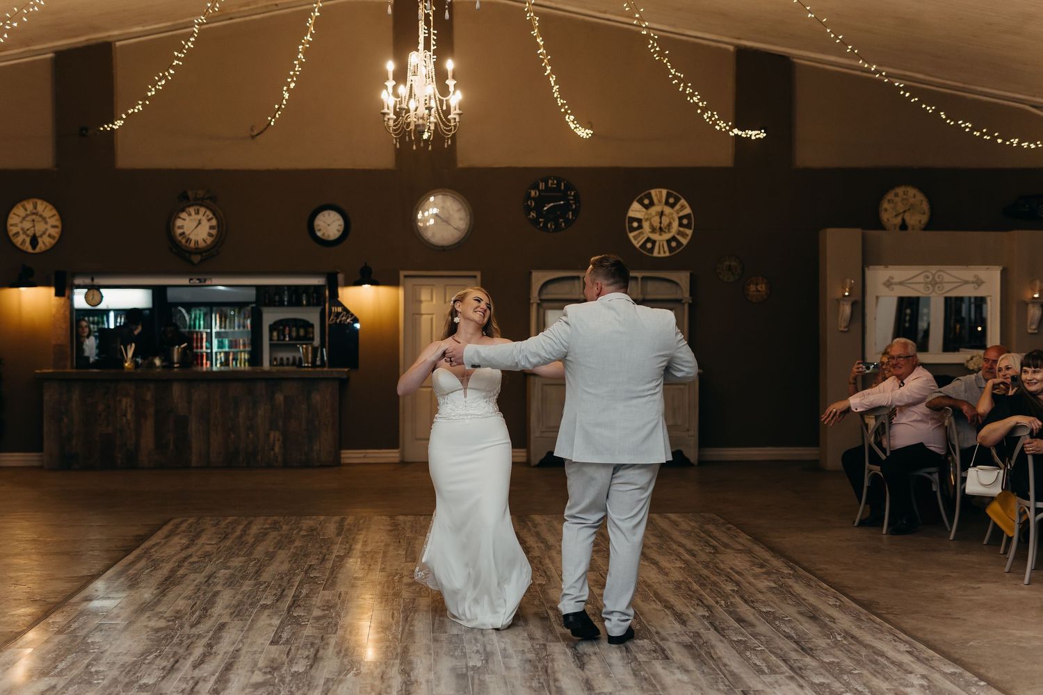Newlyweds dance in an elegant reception hall decorated with string lights and vintage decor.