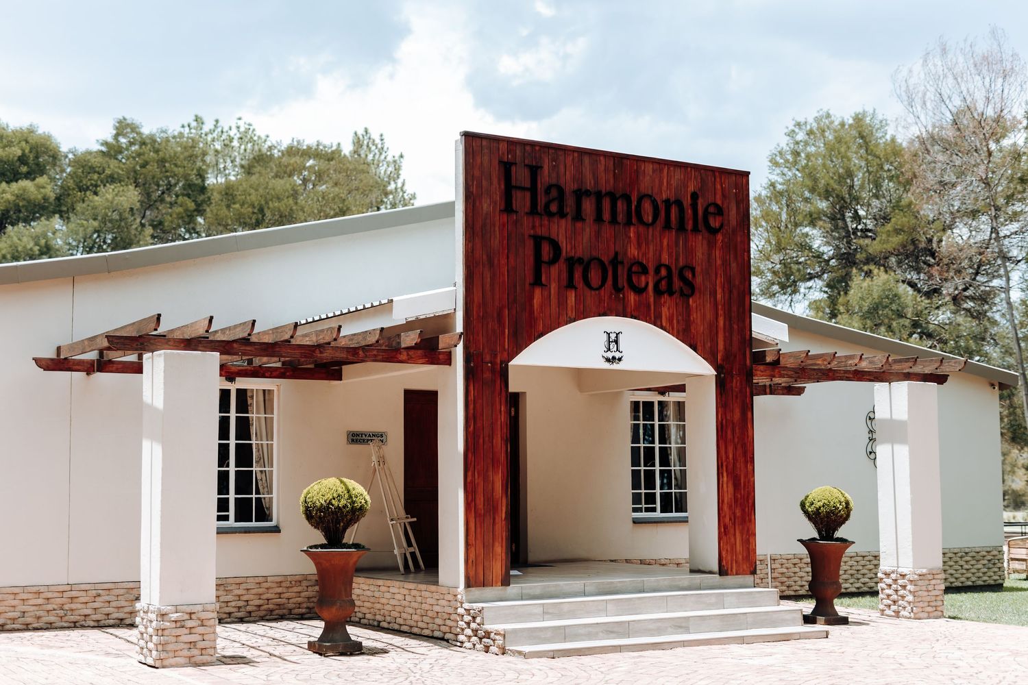 Exterior view of Harmonie Providence wedding venue with white walls and wooden pergola entrance.