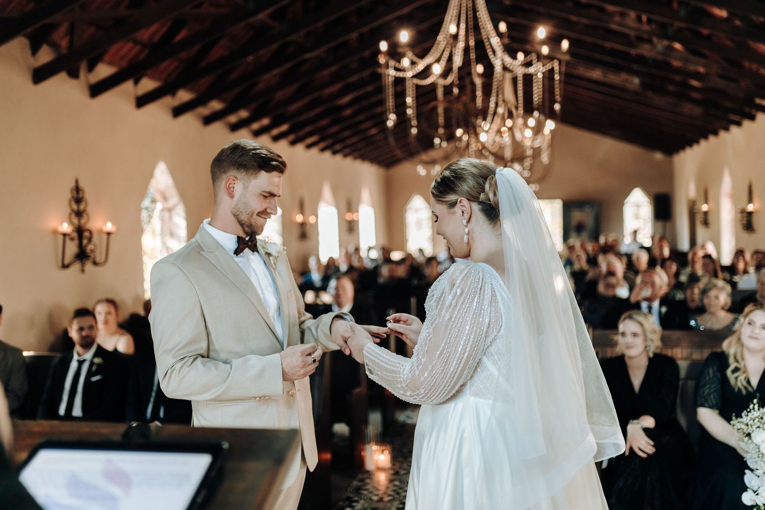 A couple participates in their ring exchange ceremony under a dramatic vaulted chapel ceiling.