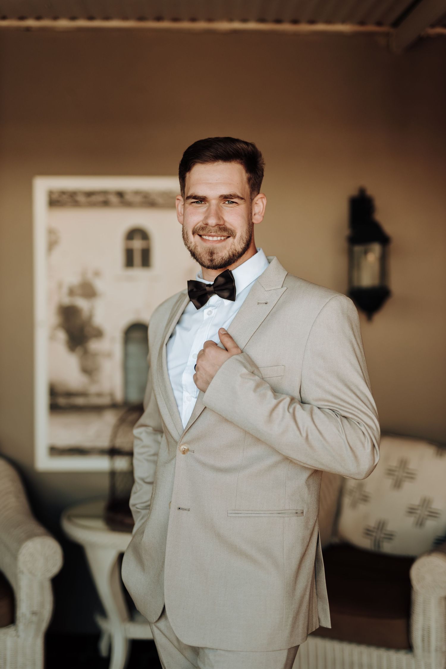 Distinguished light grey suit with black bow tie in a classically decorated room.