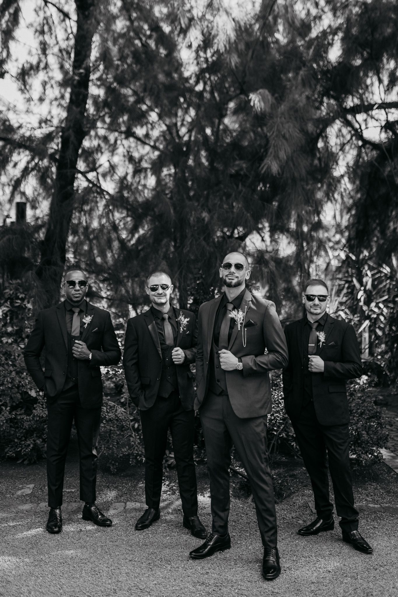 Wedding party in formal attire poses together in a black and white forest setting.