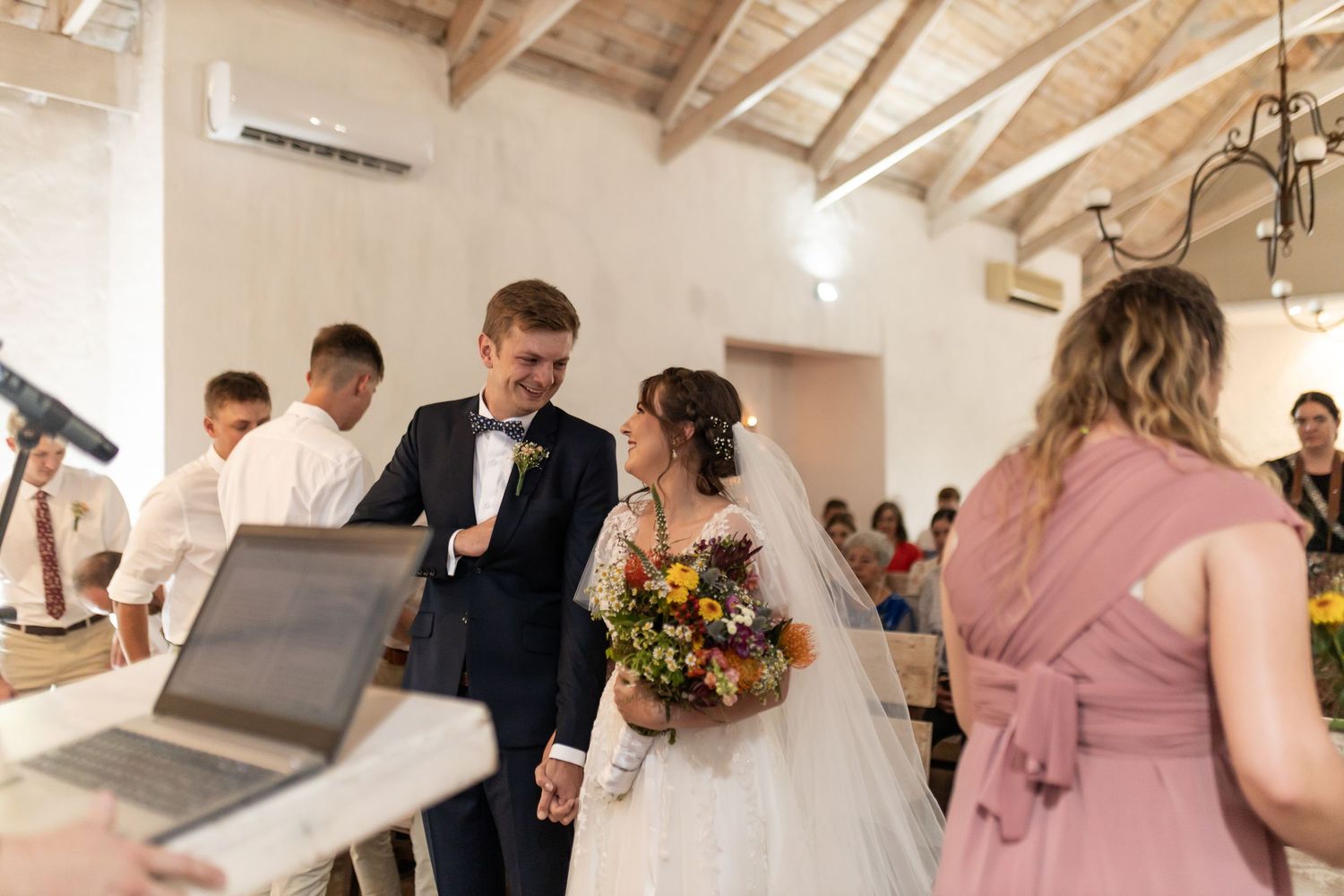 Wedding couple at altar during ceremony in rustic chapel with wooden beam ceiling.