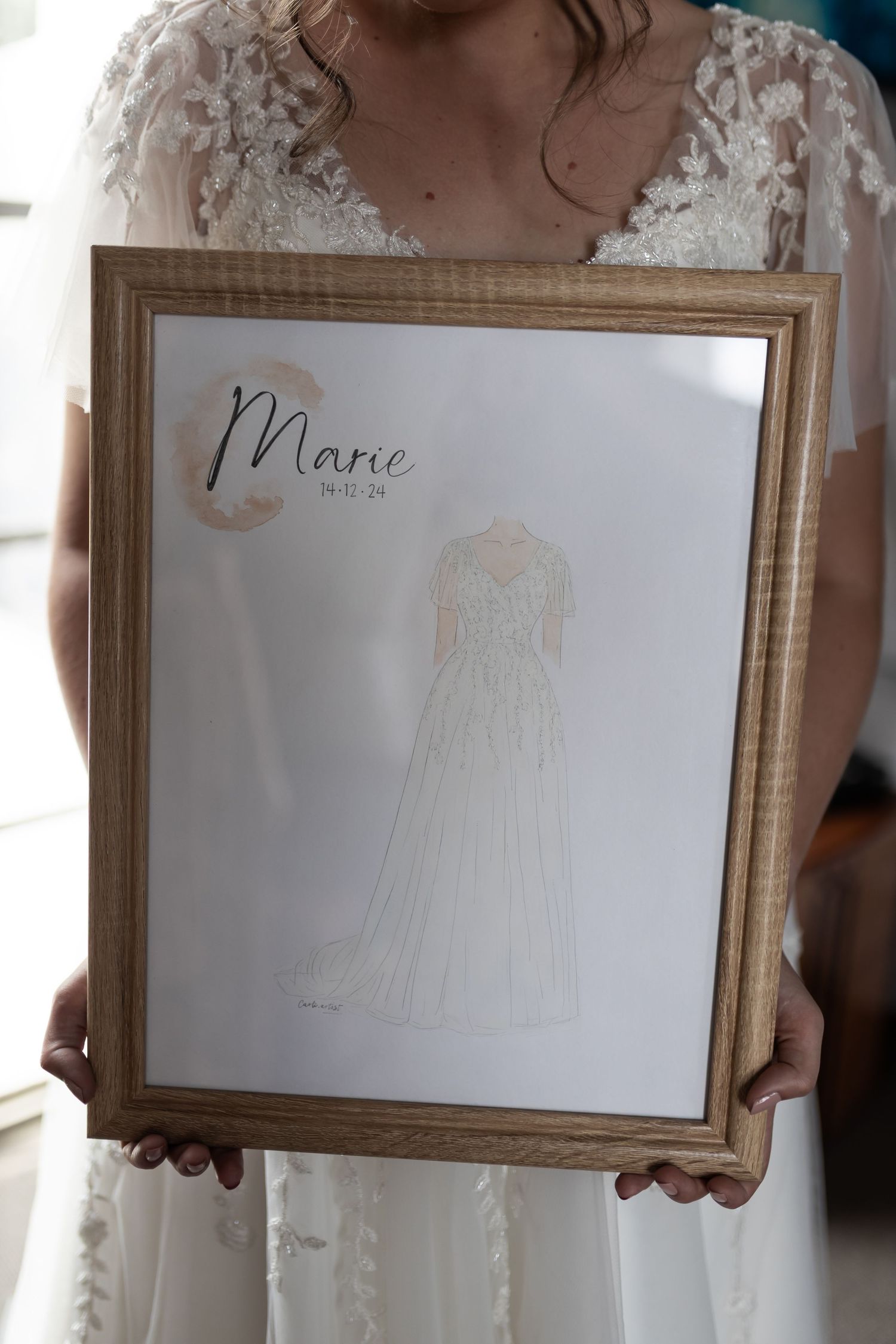 A framed wedding dress sketch is held up against a white lace gown.